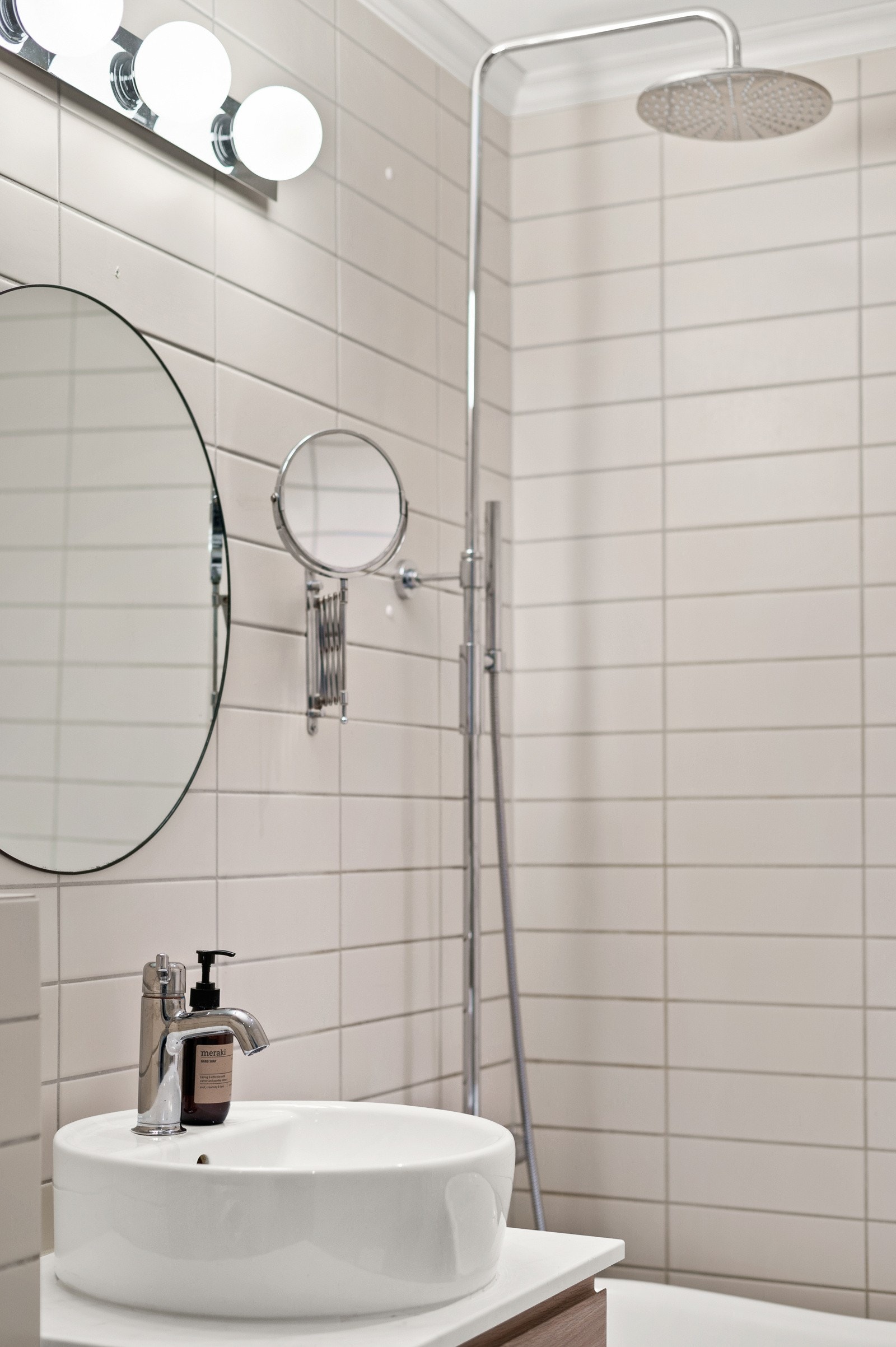 Moderne baderomsinnredning med skuffer og ovenpåliggende servant, rundt speil med belysning over. Galleribilde