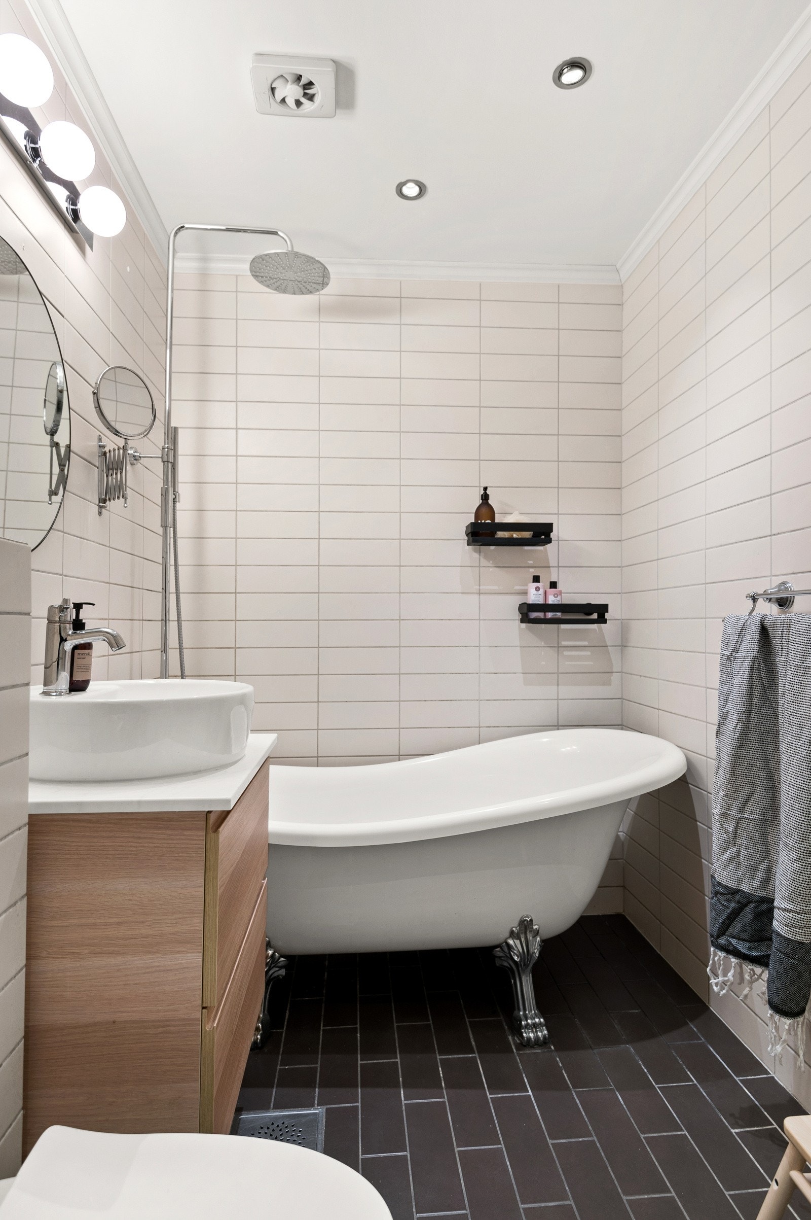 Baderommet har mørke fliser på gulv med gulvvarme, lyse fliser på veggene og himling med downlights fra 2012. Elektrisk avtrekksvifte i himling. Galleribilde