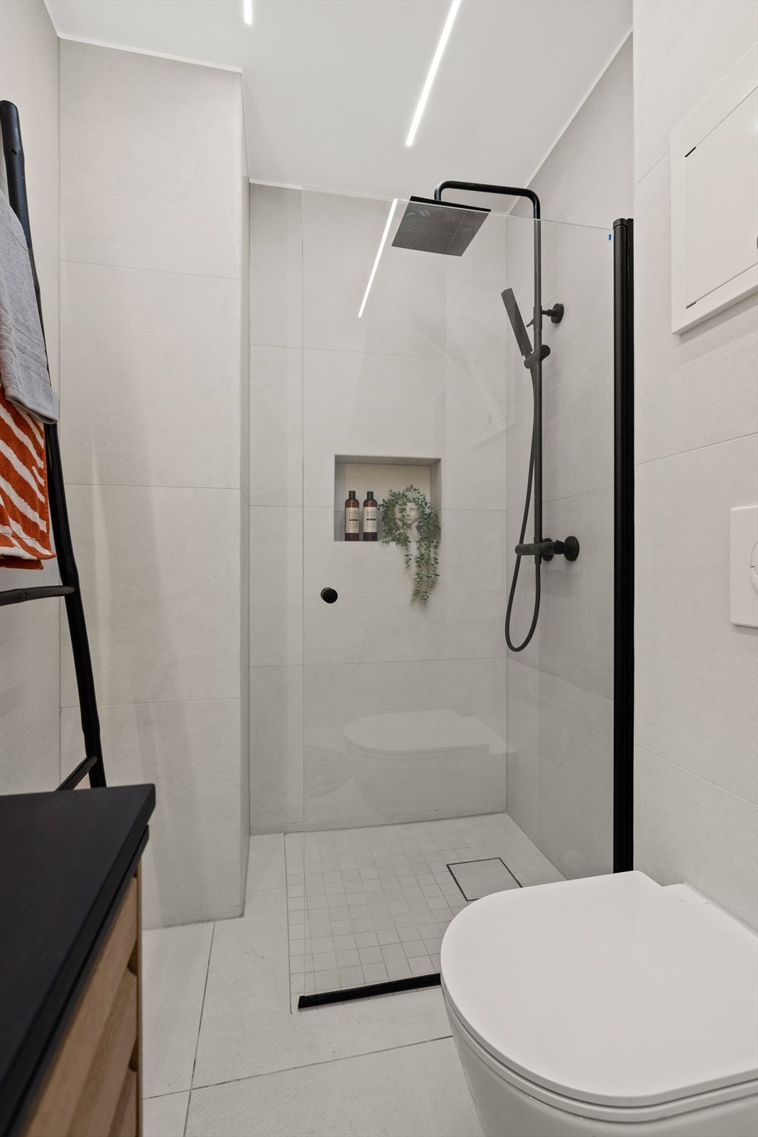 Baderomsinnredningen bestående av servant med underskap, vegghengt speil med lys, dusjhjørne med innfellbar dør og vegghengt toalett Galleribilde