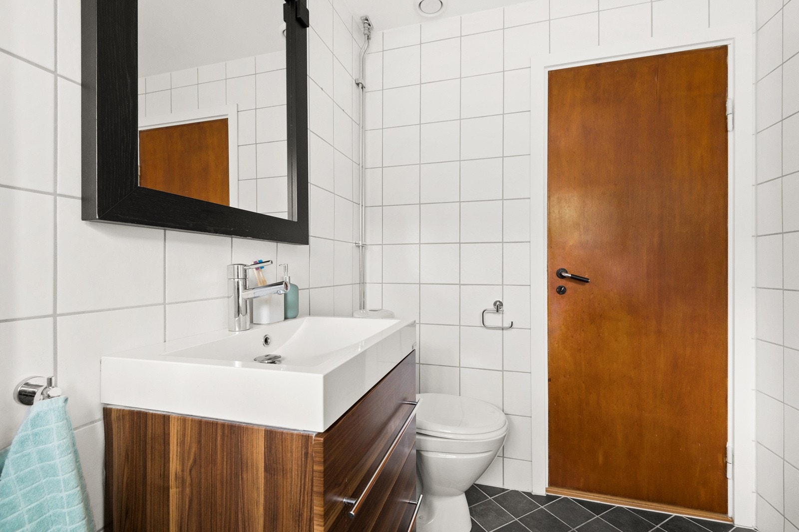 Baderommet har mørke fliser på gulv med gulvvarme, lyse fliser på veggene og et vindu som slipper inn deilig dagslys. Galleribilde