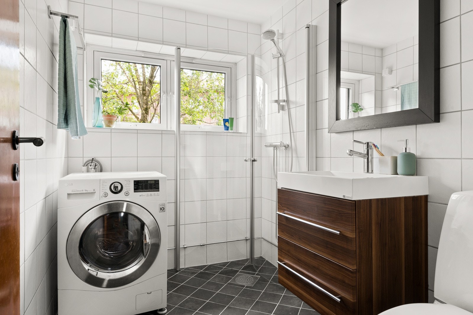 Moderne baderomsinnredning med skuffer og heldekkende servant, stort speil med belysning over. Baderommet er også utstyrt med dusjhjørne med innfellbare glassdører og gulvmontert toalett. Galleribilde