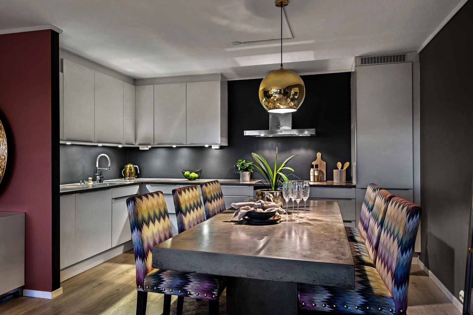 Kjøkkenet har et stilrent uttrykk med hvite, glatte fronter og mørk farge på vegg Galleribilde