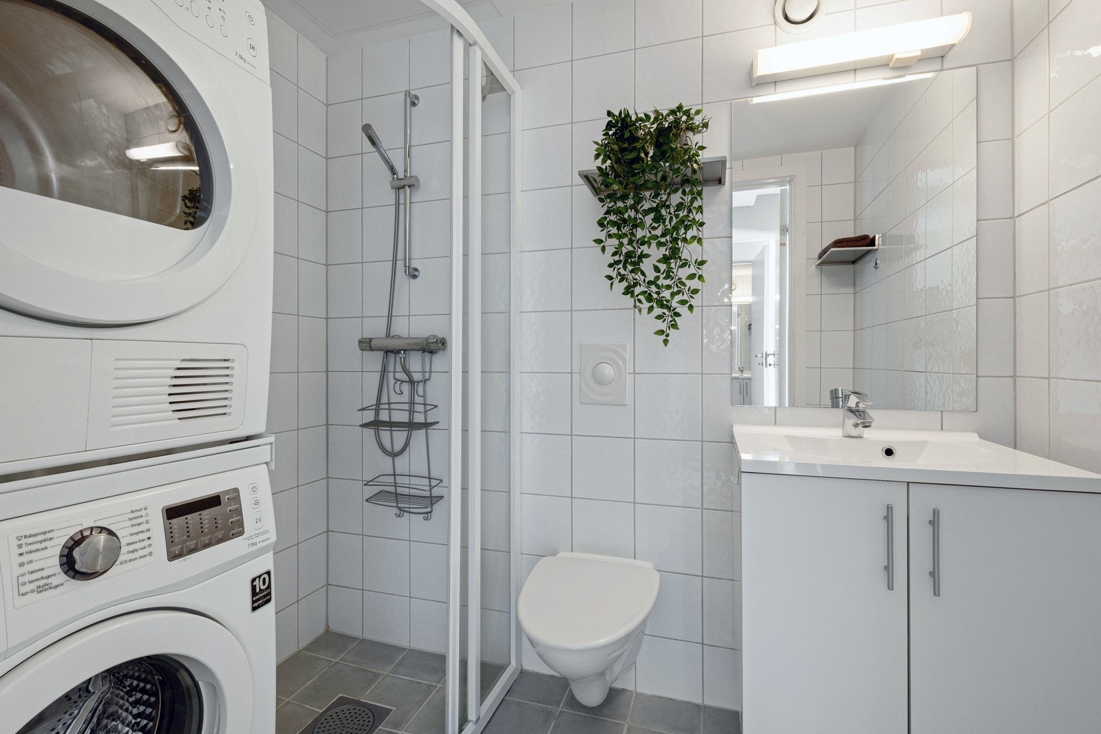 Badet i hoveddelen fremstår som velholdt og pent, og rommet har hvite fliser på veggene og grå fliser på gulv med gulvvarme. Galleribilde