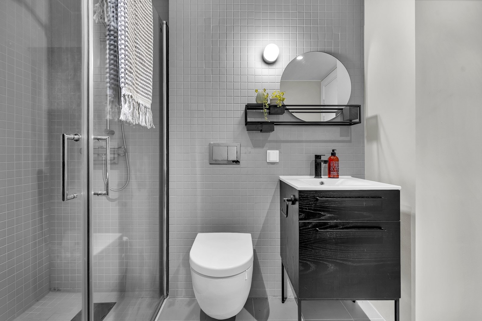 Baderommet er innredet med servant, hylle med speil, veggfestet toalett og dusj med innfellbare dører i herdet glass. Galleribilde