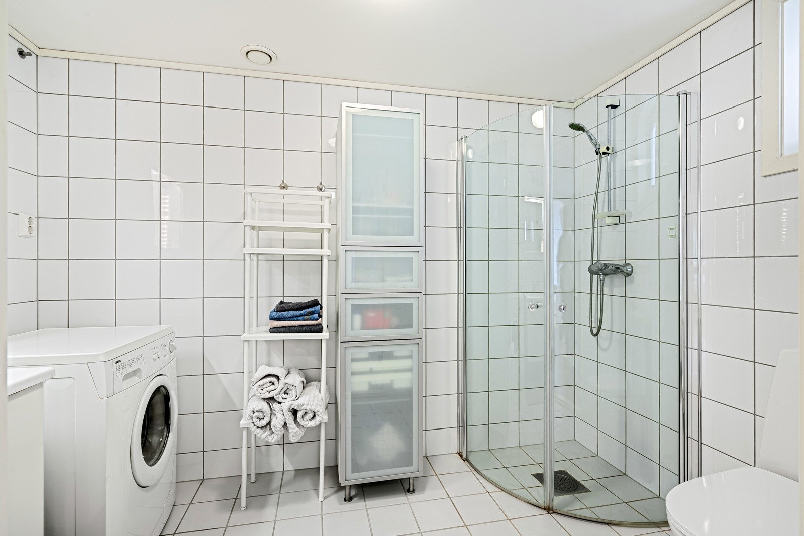 Badet er utstyrt med vegghengt toalett, innfellbare dusjdører, opplegg for vaskemaskin og varmekabler i gulv Galleribilde