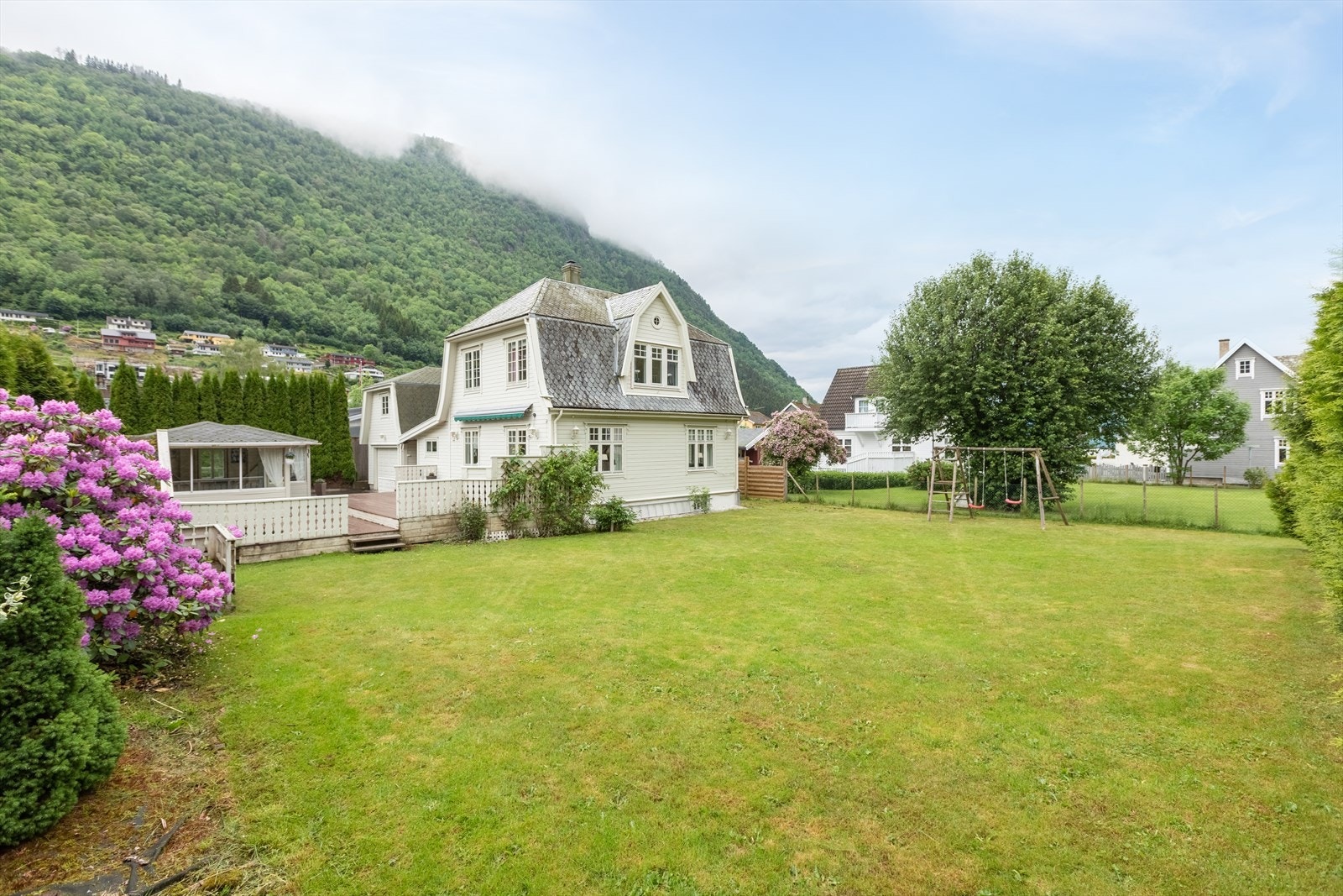 Flat opparbeida tomt, med plen , gjerde mot nabo, prydbusker og asfalt i innkøyrsle Galleribilde