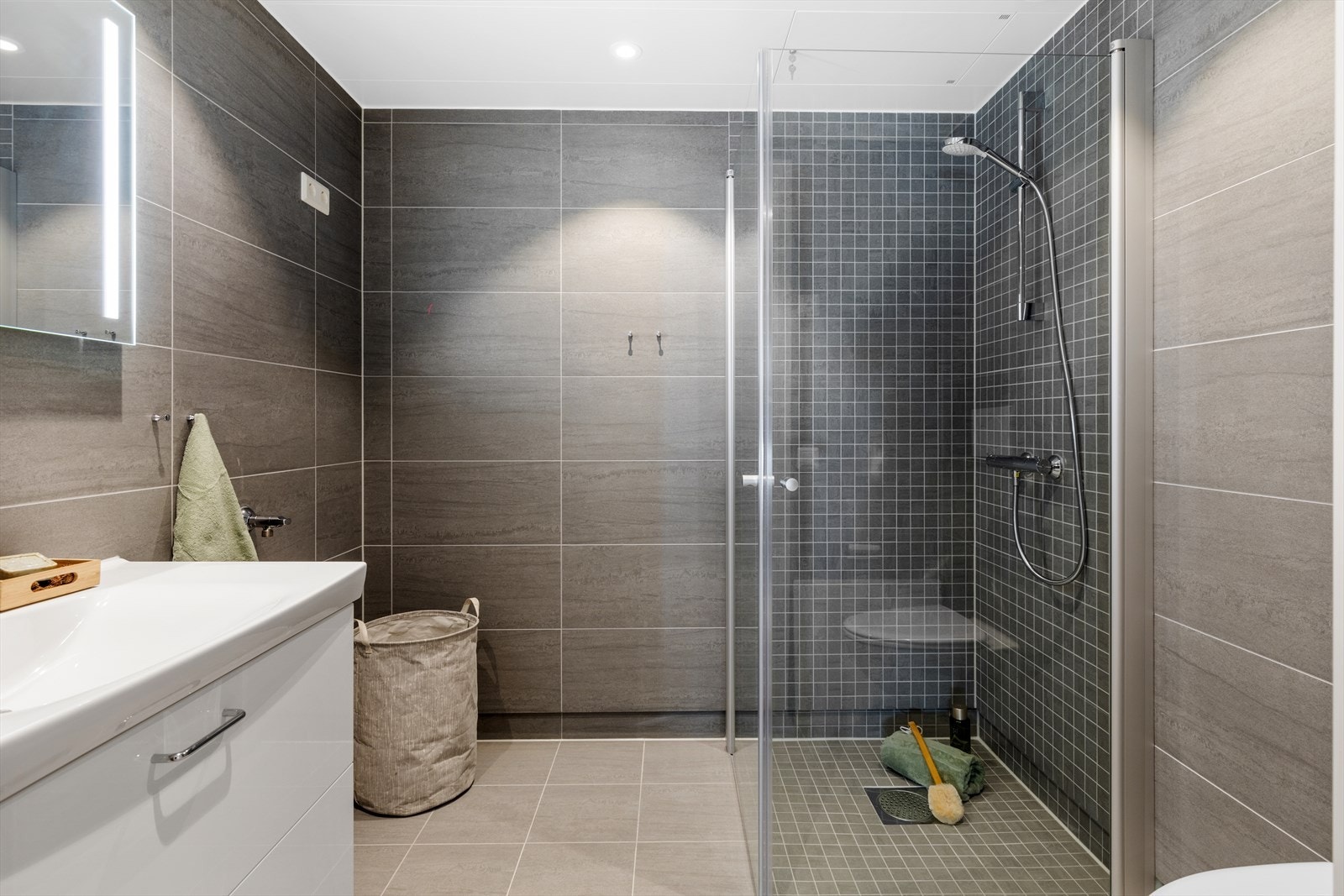 Badet er innredet med servantinnredning, toalett, dusjhjørne, opplegg for vaskemaskin og downlights. Galleribilde