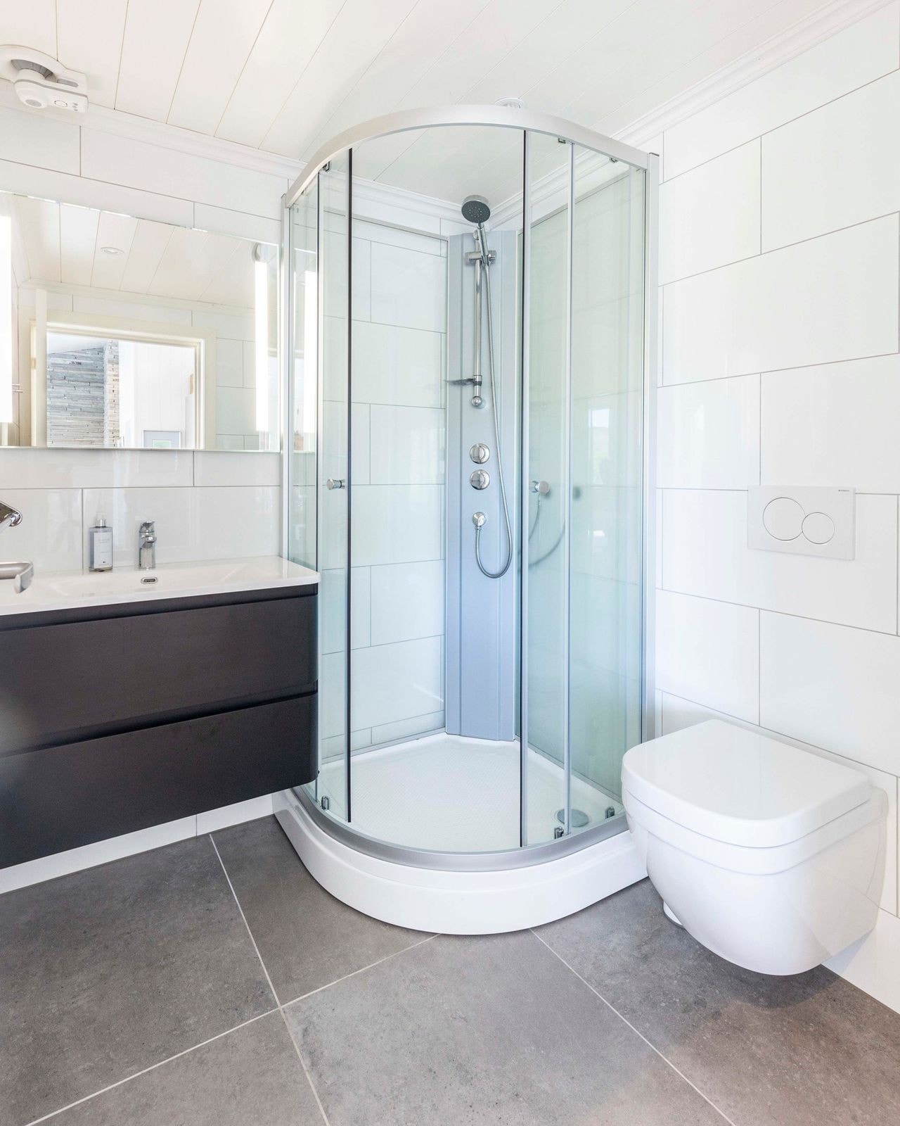 Flislagt bad med varmekabler, med vegghengt toalett, LED downlights, speil med dimbare LED-lys, samt servantskap og dusjkabinett. Hans Grohe blandebatteri Galleribilde
