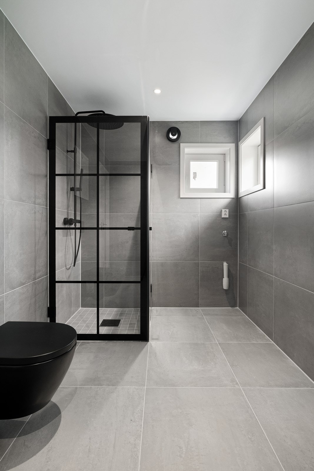 Videre har badet nedsenket dusjnisje med fliser i størrelse 7x7. Her er det 180 hjørnedusj med sorte, matte hengsler og klart glass. Galleribilde