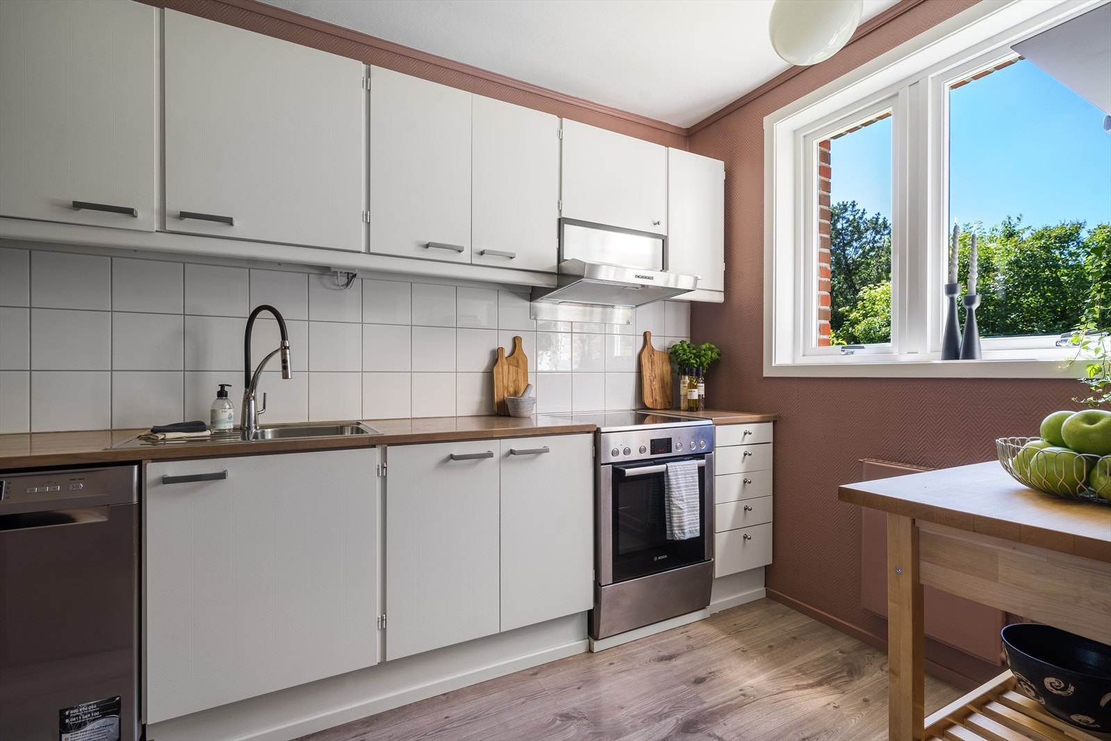 Koselig og adskilt kjøkken med innredning med hvite fronter, nisje til komfyr og opplegg til oppvaskmaskin Galleribilde