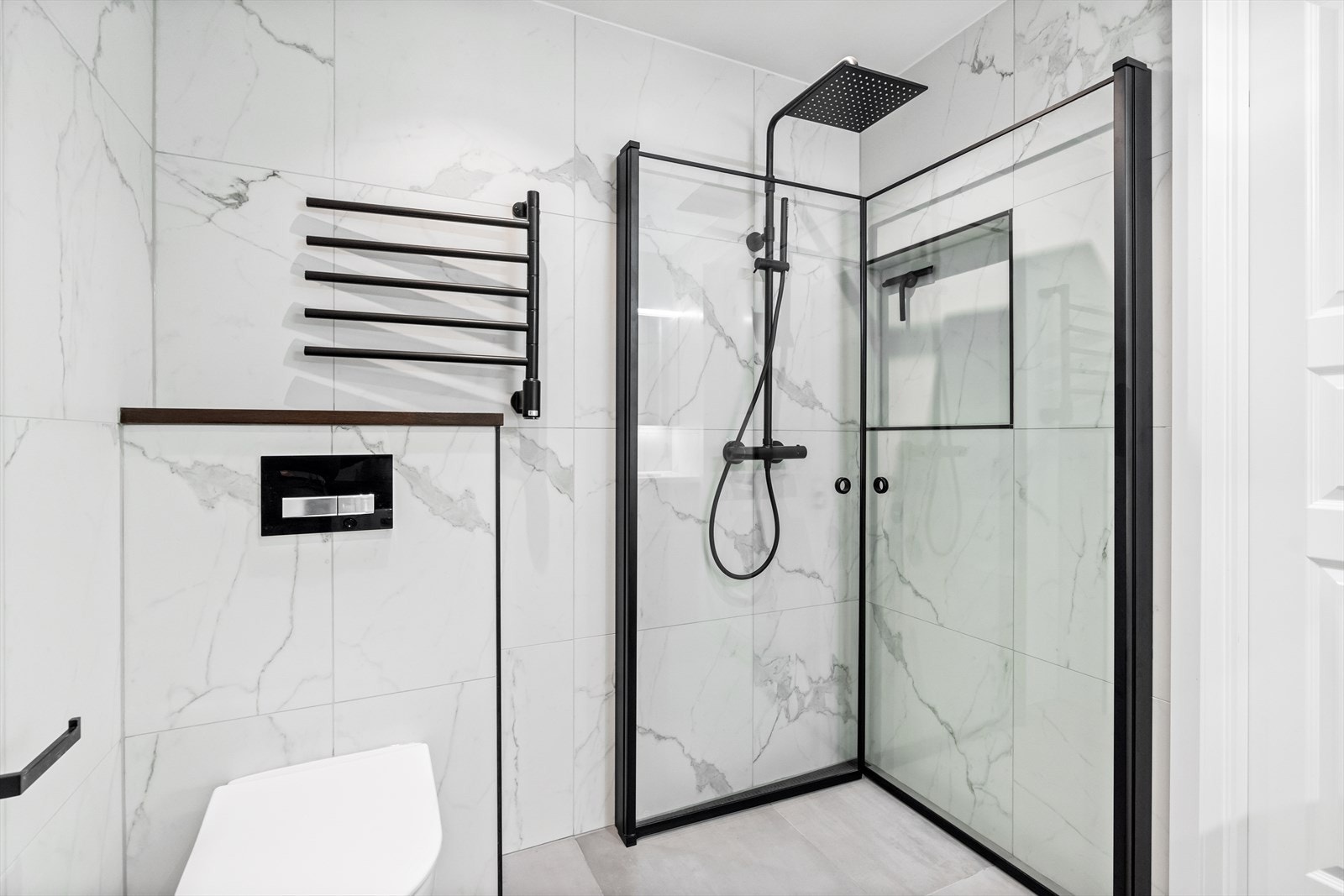 Badet har downlights i himling og gulvvarme på bad. Rommet har stilren servantseksjon med underliggende skuffer, vegghengt toalett og et dusjhjørne med innfellbare glassvegger og regnfallsdusj. Galleribilde