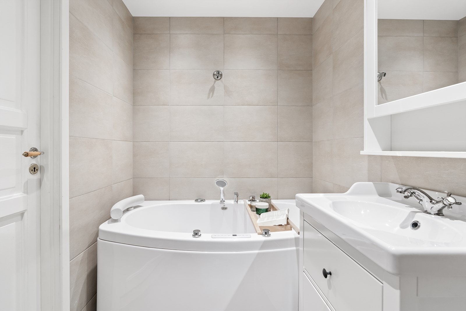 Badet er innredet med badekar, servant med underliggende skuffeseksjoner og vegghengt toalett. Flisene er holdt i nøytrale, tidløse farger i en nydelig beige-tone, og det er brune gulvfliser med gulvvarme. Galleribilde