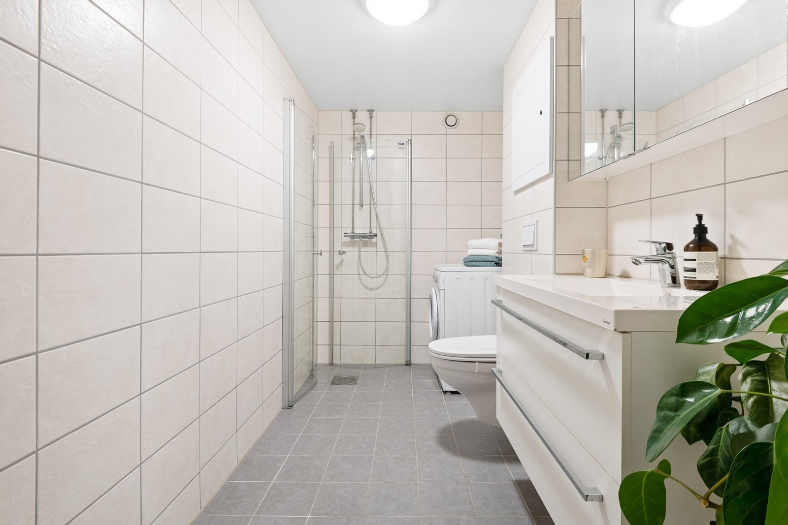 Badet er innredet med veggmontert wc, dusjplass med inn-utadslående dusjvegger, servant med ettgreps
blandebatteri i innredning og opplegg for vaskemaskin Galleribilde