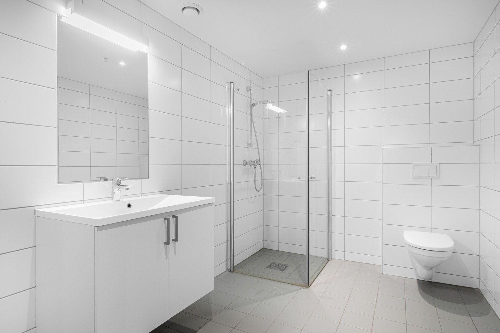 Smakfullt bad med flislagte overflater og varmekabler i gulv, nytt i 2018. Innredningen består av moderne servantmøblement med underskap, speil og vegghengt toalett. Videre har badet et separat dusjhjørne med innfellbare glassdører og hånddusj. Galleribilde