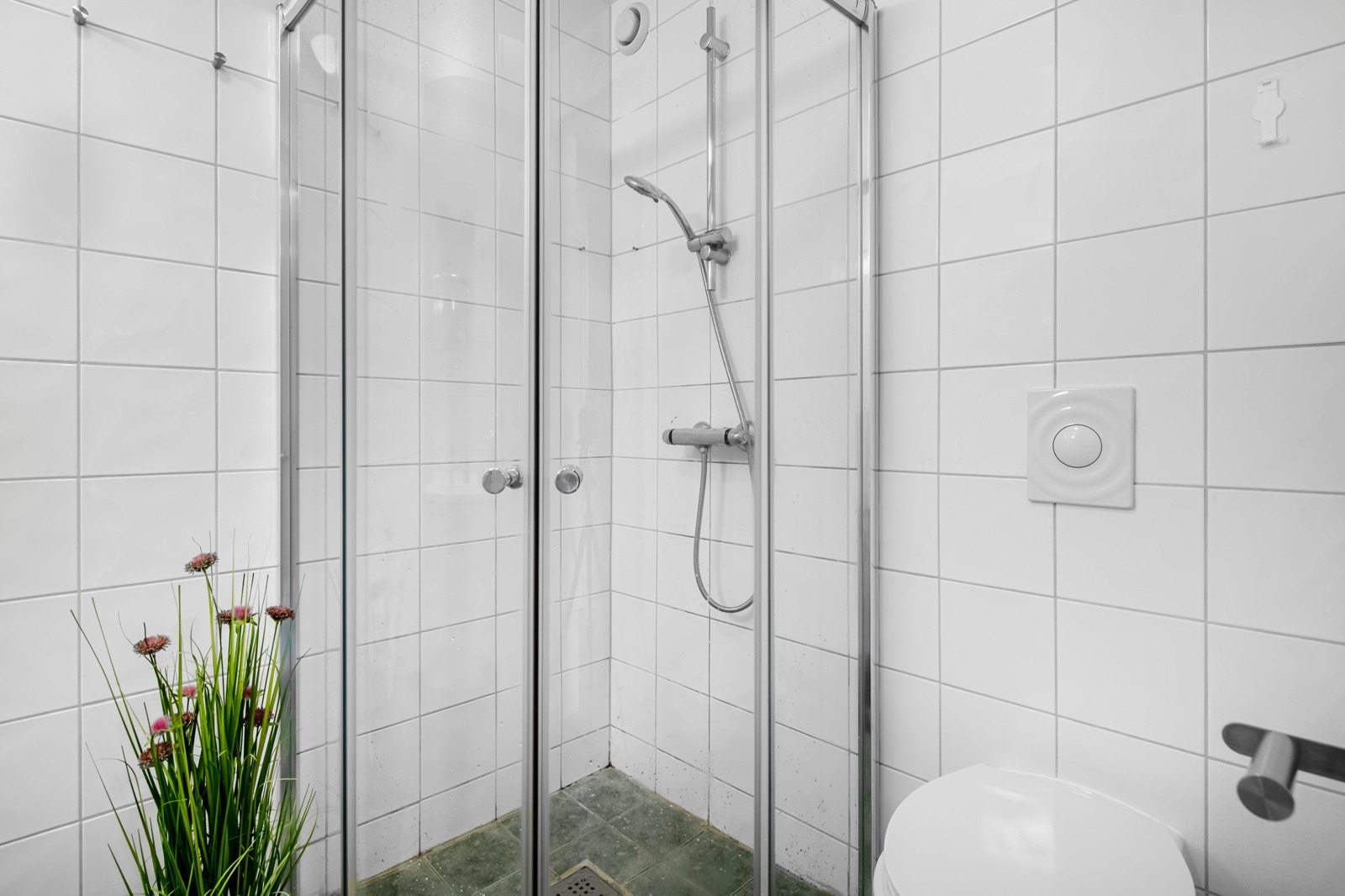 Badet ligger i første etasje og har grå fliser på gulvet, lyse fliser på veggene, gulvvarme, veggmontert toalett og opplegg for vaskemaskin. Galleribilde