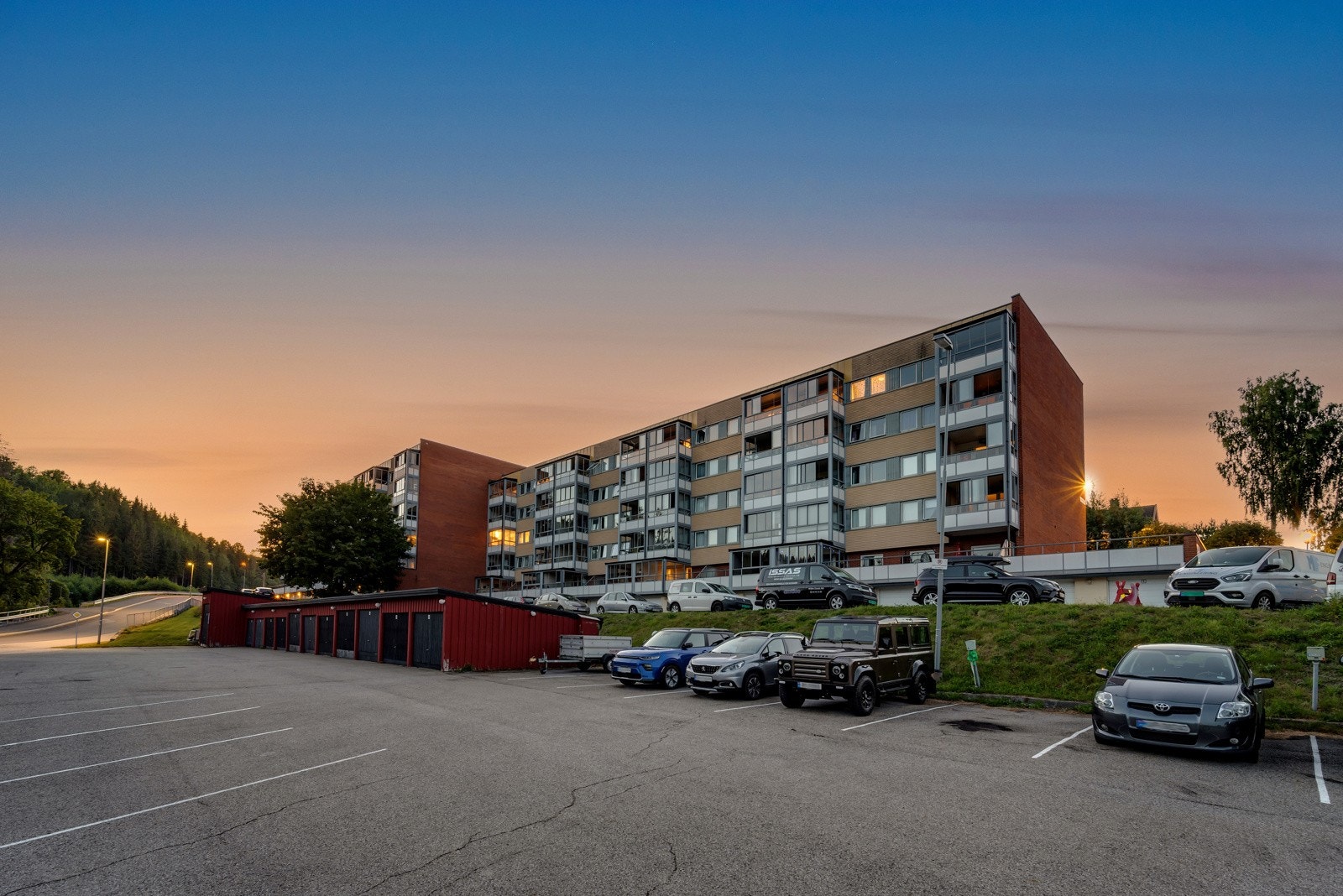 Parkeringsplass på borettslagets tomt og fasade av blokkens bakside. Galleribilde