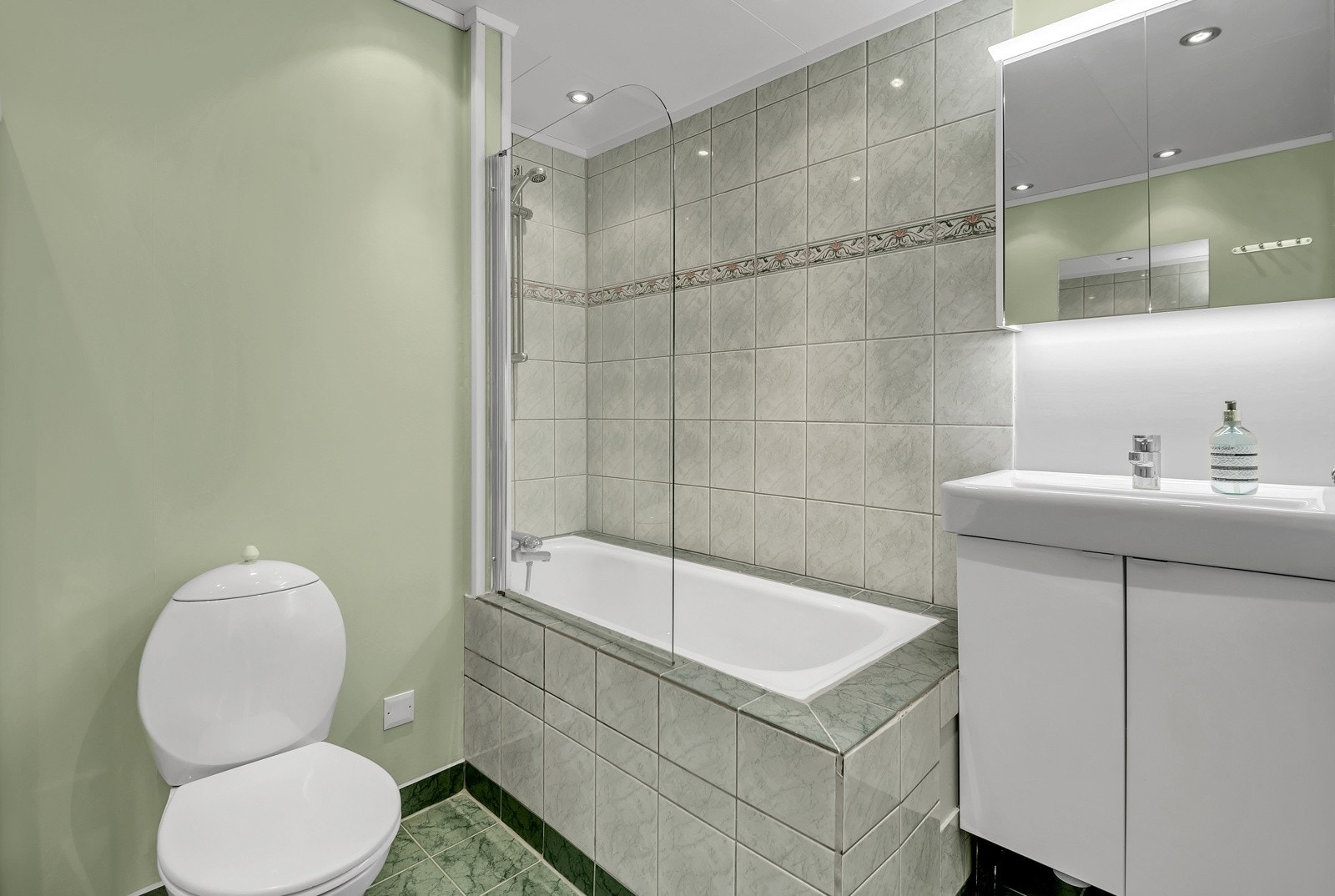 Bad/WC, ca. 5 m². Delvis flislagt bad som er innredet med toalett, servant, underskap og innbygd badekar med dusjvegg. Galleribilde