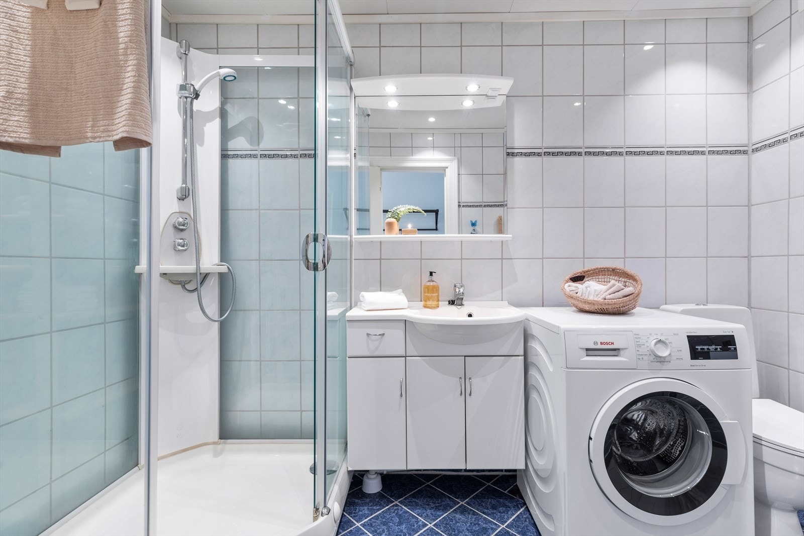 Badet er utstyrt med servant, underskap og tilhørende speil, dusjkabinett, toalett og opplegg for vaskemaskin. Galleribilde