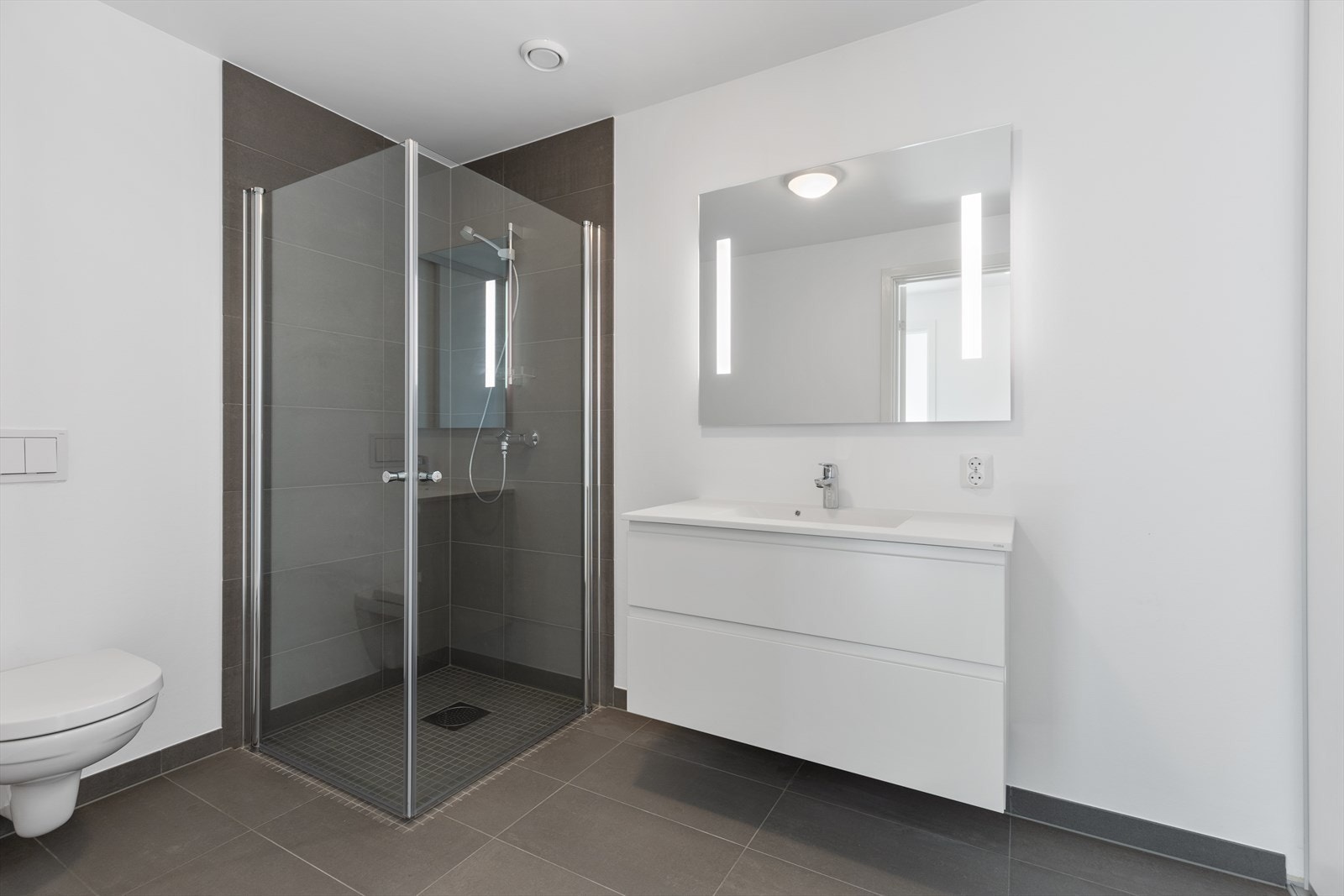 Tiltalende baderom med vegghengt toalett, baderomsinnredning med speil og dusjnisje med glassvegger. Vaskeromsnisje med skyvedører. Galleribilde