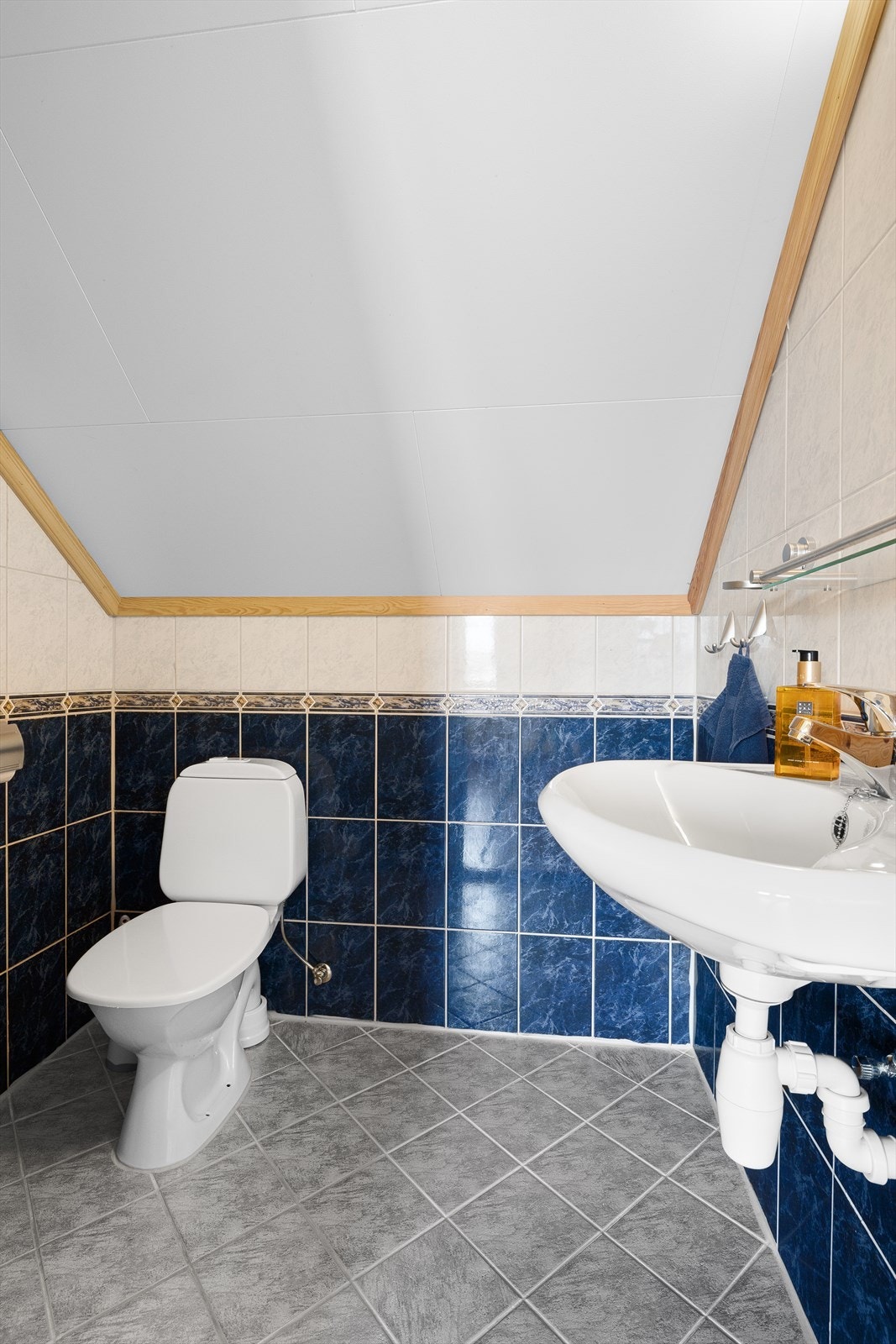 Badet har fliser på gulv og vegger. Det er innredet med toalett, baderomsinnredning med vask og opplegg for dusj. Galleribilde