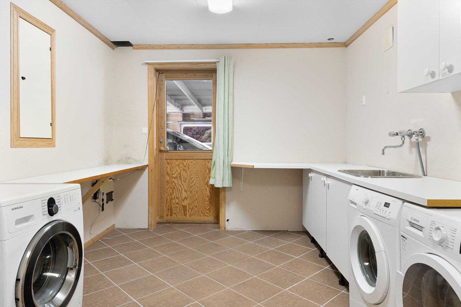 Separat vaskerom med gulvfliser og sponplater på vegger. Rommet er innredet med skyllekar i stål og opplegg for vaskemaskin. Galleribilde