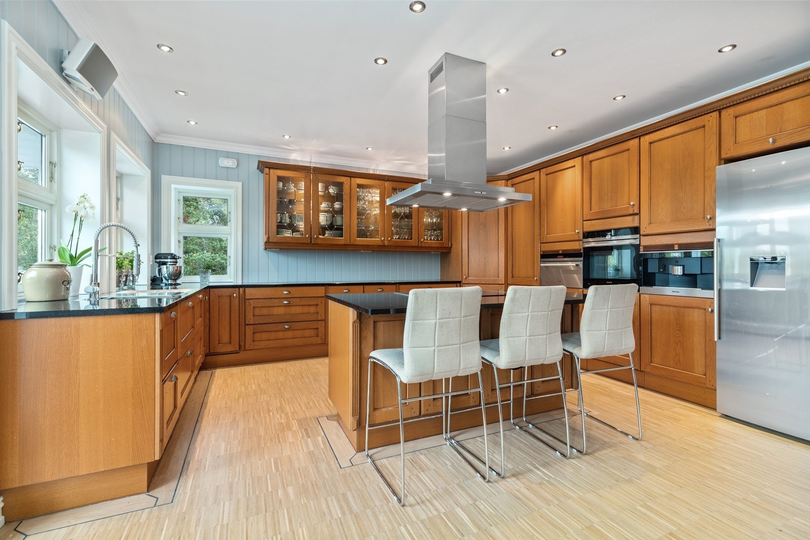 Innredningen fra JKE design av typen Lyon har profilerte eikefronter, vitrineskap og granitt benkeplate med nedfelt oppvaskkum. De flotte tykke granittplatene på alle flatene i kjøkkenet gir kjøkkenet en fin kvalitet og gjør det lett å renholde. Galleribilde