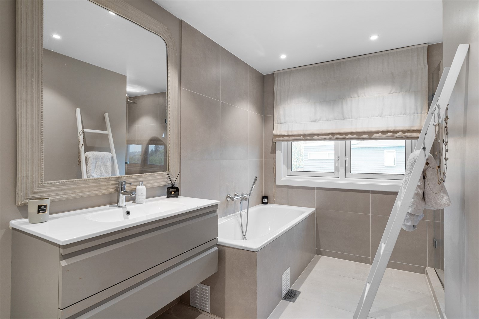 Badet er utstyrt og innredet med servantskap med skuffer og heldekkende servant. Vegghengt toalett med innebygget sisterne. Dusjnisje med regnfallsdusj og dør i herdet glass. Innebygget badekar med veggmontert blandebatteri med hånddusj. Galleribilde