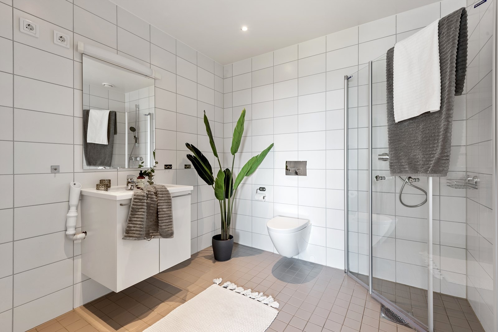 Innredning med heldekkende servant på benkeskap med glatte fronter, speil med lys, vegghengt toalett og dusj i hjørnet bak svingbare glassvegger. Opplegg for vaskemaskin. Galleribilde