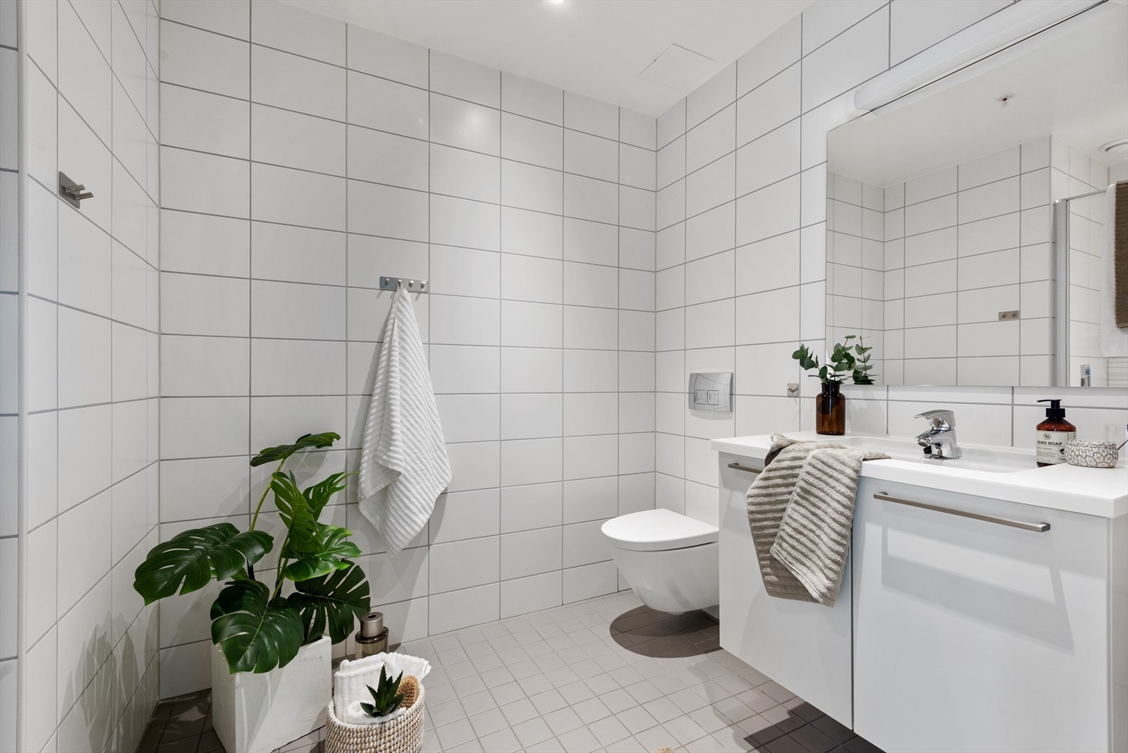 Bad v/entrèen er flislagt med underliggende varmekabler og inneholder heldekkende servant på benkeskap, speil med lys og vegghengt toalett. Galleribilde