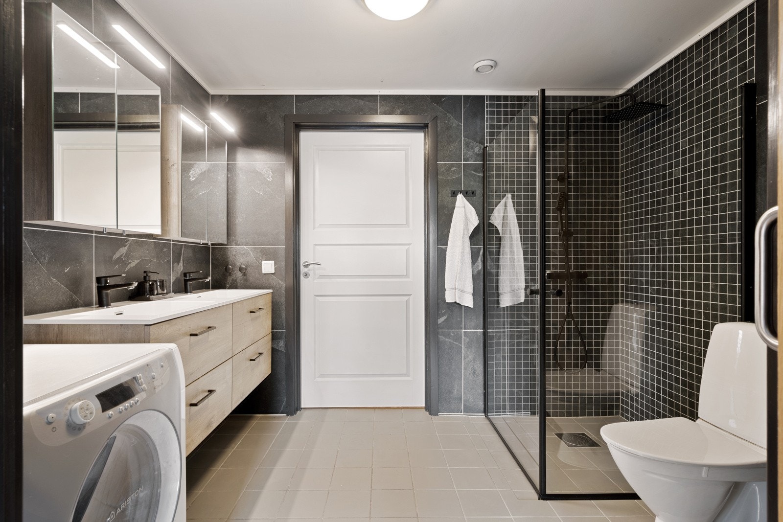 Badet er utstyrt med innfellbare dusjdører, dobbel servanttopp med underskap, opplegg for vaskemaskin og varmekabler i gulv Galleribilde