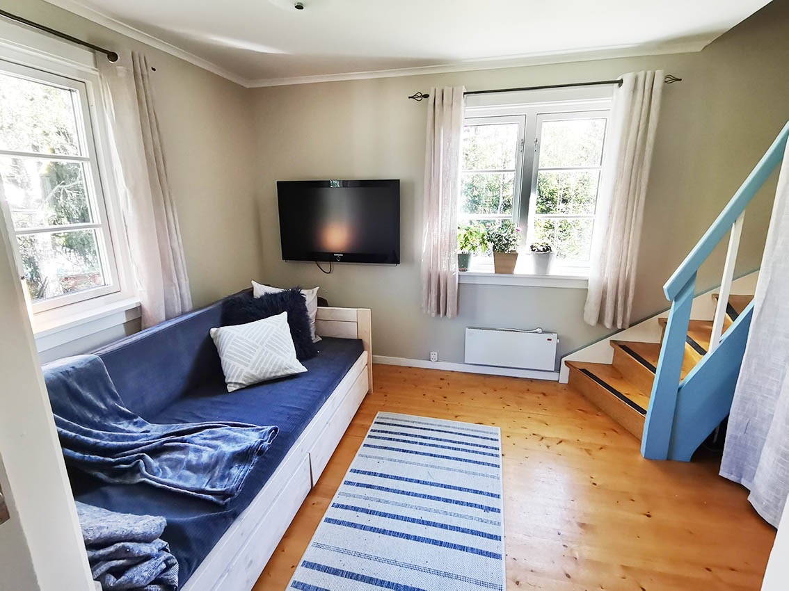 Rom med TV flatskjerm, sovesofa og trapp til 2 etg Galleribilde