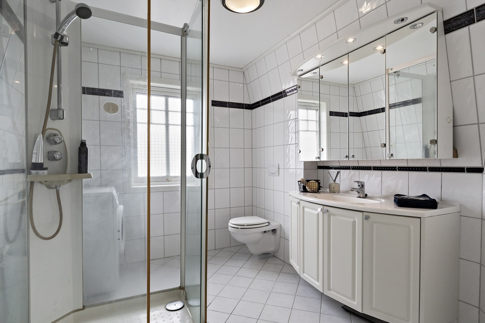 Helfliset bad med malt slett himling. Badet er innredet med vegghengt toalett, servant i skapinnredning med speilskap, dusjkabinett og opplegg for vaskemaskin. Galleribilde