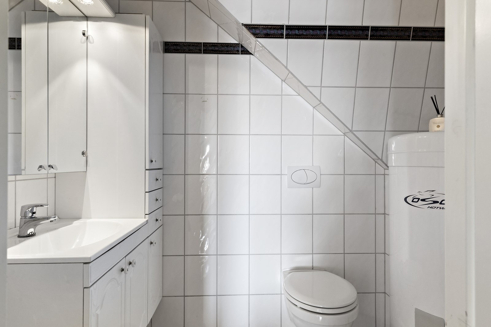 Wc-rom med fliser på vegg og gulv, samt malt slett himling. Wc-rommet er innredet med servant i skapinnredning og vegghengt toalett. Galleribilde