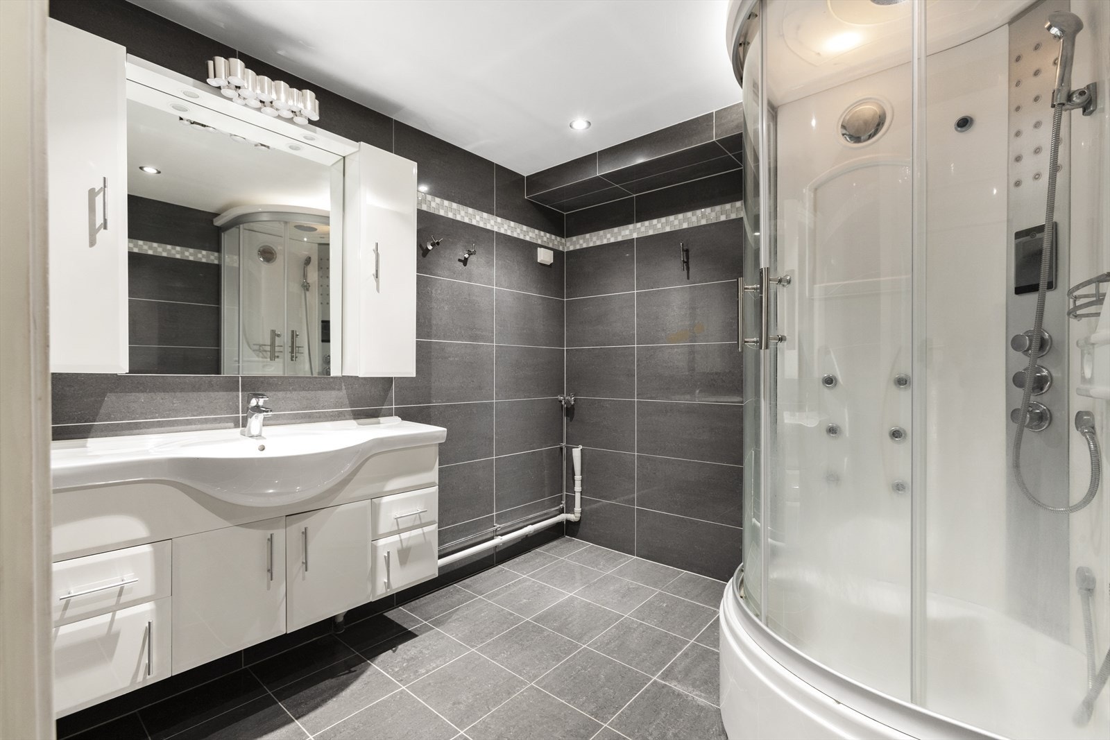 Pent flislagt bad fra 2009 med god plass til dusjkabinett. Innredning bestående av servantskap i hvit glatt utførelse med heldekkende servant og overskap. Det er også opplegg for vaskemaskin. Galleribilde