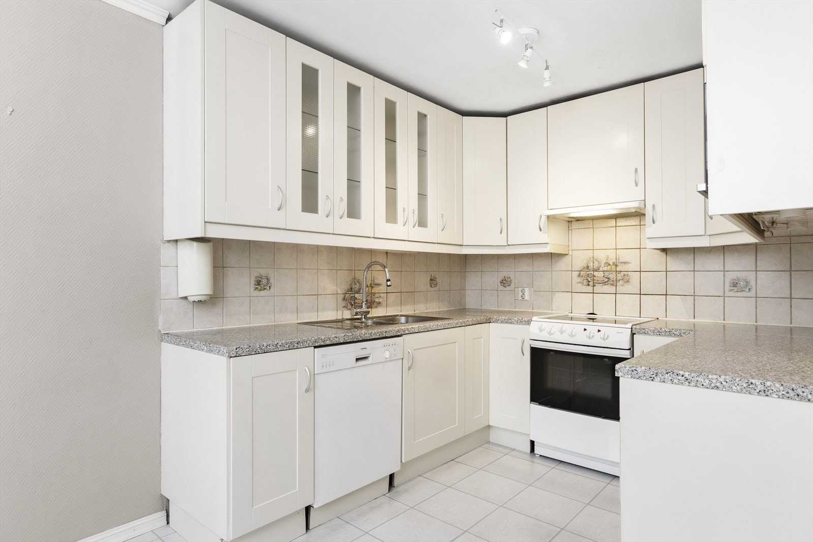 Kjøkkeninnredning med hvite klassiske fronter. Benkeplate i laminat med nedfelt oppvaskkum med 1-greps blandebatteri. Fliser på vegg over benk. Galleribilde