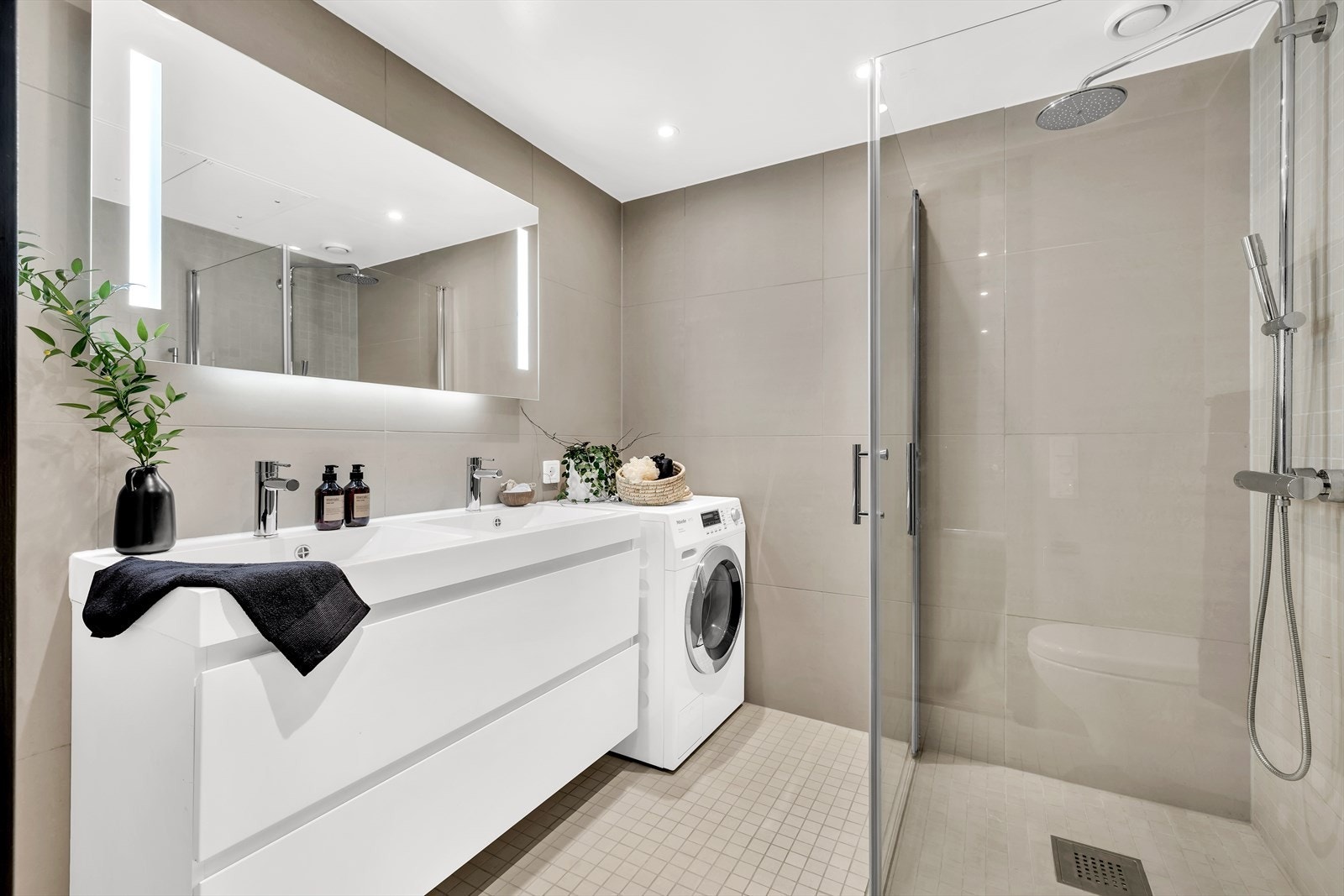 Hovedbadet er innredet med delikate, beige fliser. Langs den ene veggen og på gulvet er det lagt mosaikkfliser. Galleribilde