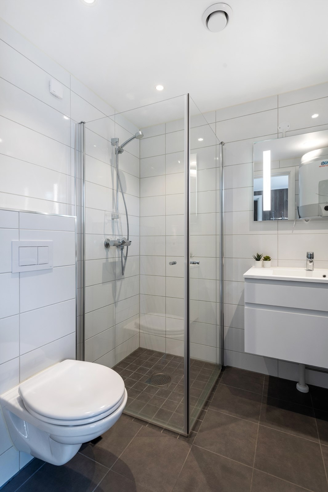 Med vegghengt klosett, dusjhjørne, innredning med skuffeseksjon samt opplegg for vaskemaskin. Galleribilde