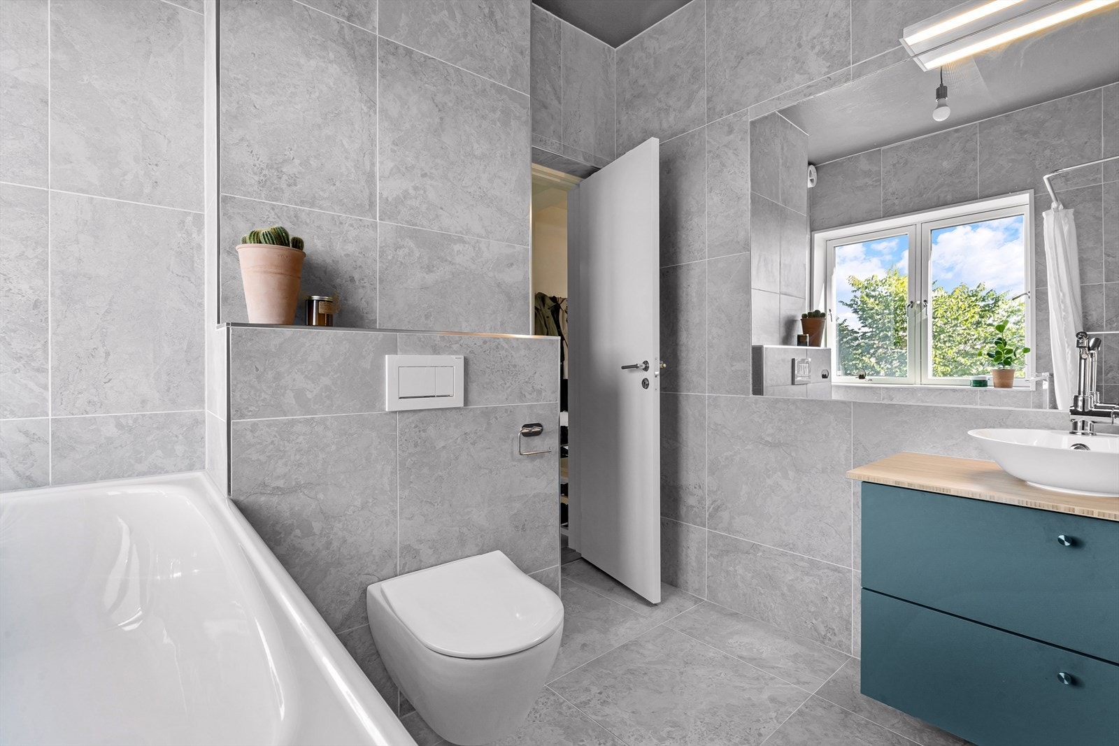 Baderommet inneholder vegghengt toalett, servant med skuffer til oppbevaring, regnfallsdusj og badekar. Galleribilde