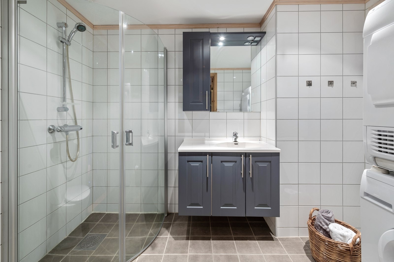 Badet har flislagt gulv og vegger, malt glatt overflate i himling. Badet er utstyrt med servantinnredning, håndvask, toalett, dusj med vegger/dører i glass. Galleribilde