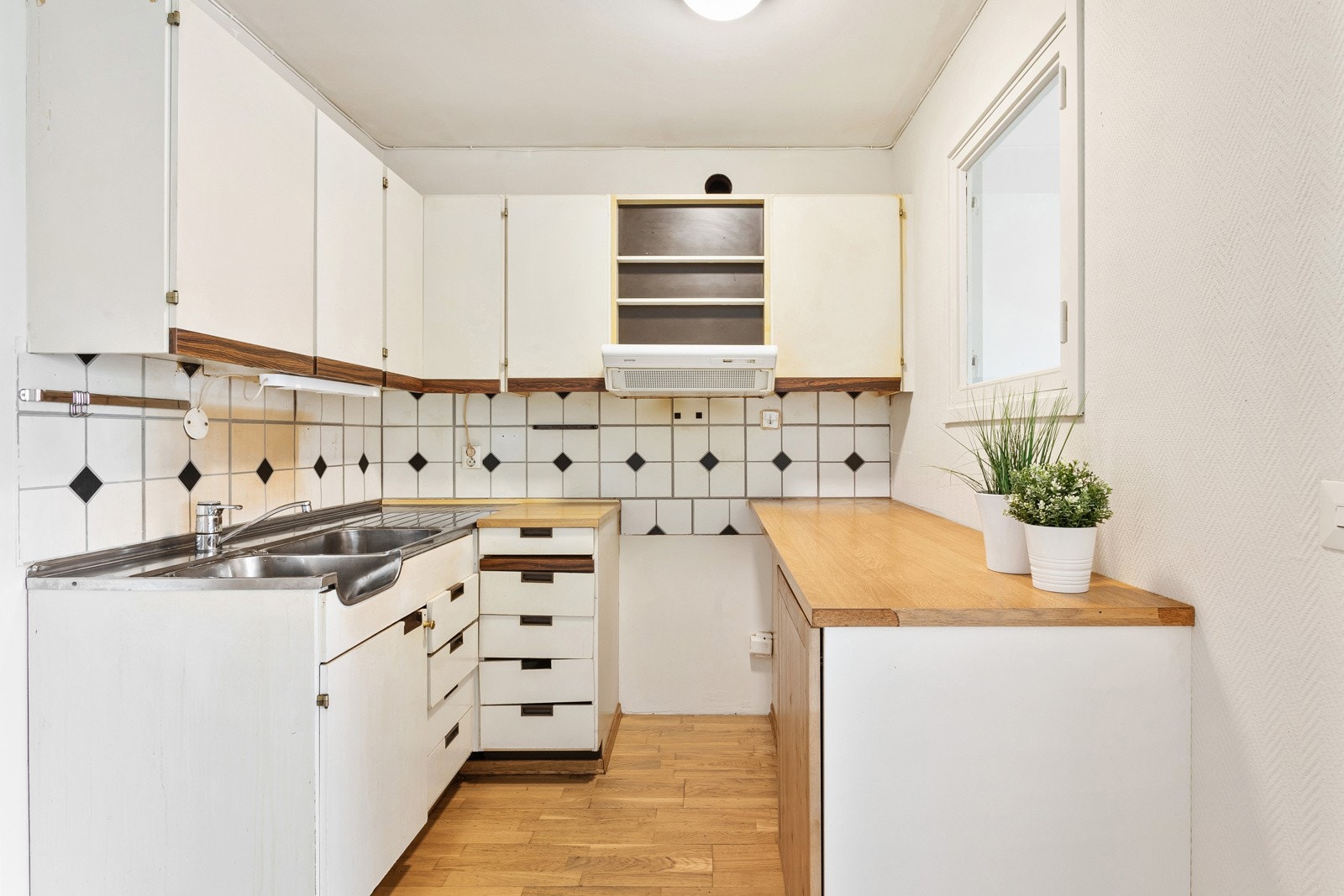 Kjøkkeninnredning med glatte fronter og stor bruksslitasje. Belysning under overskap. Fliser på vegg over benkeskap. Laminat benkeplate med kum i rustfritt stål. Kullfilterventilator. Galleribilde