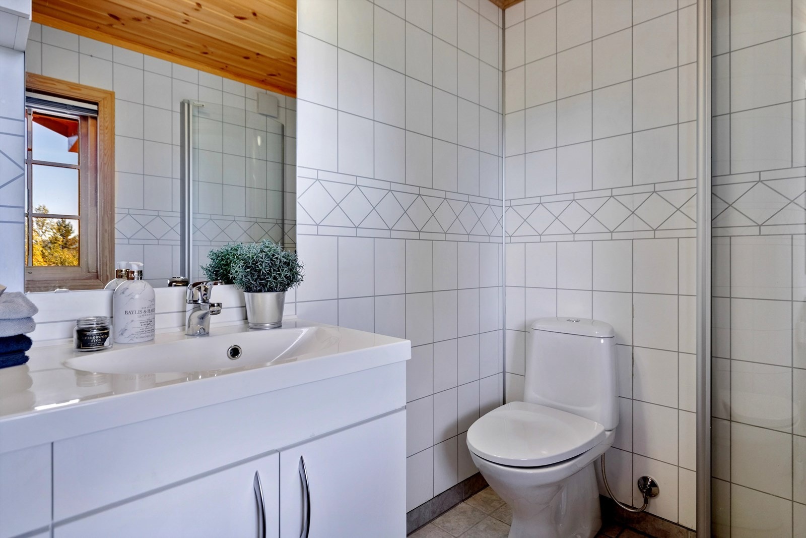 Badet er innredet med baderomsinnredning med servant, dusjvegger og gulvmontert toalett. Galleribilde