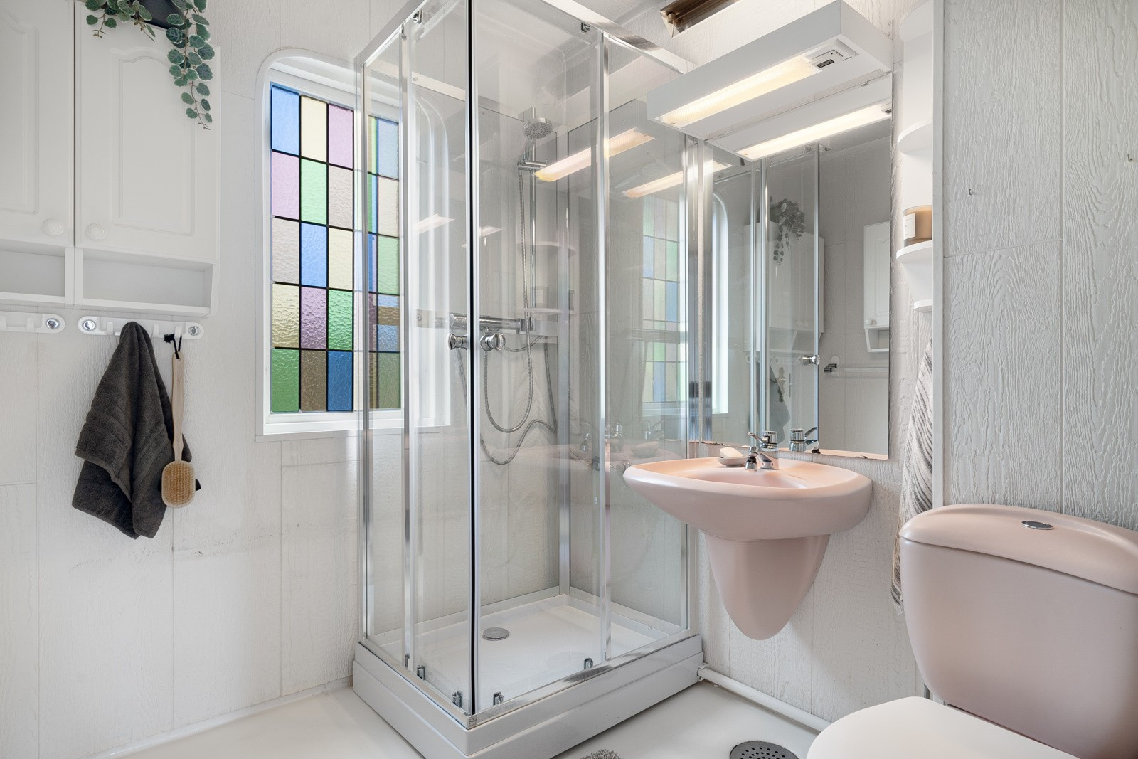 Badet har vinylbelegg på gulv, vegghengt vask og veggmontert speil med lys.