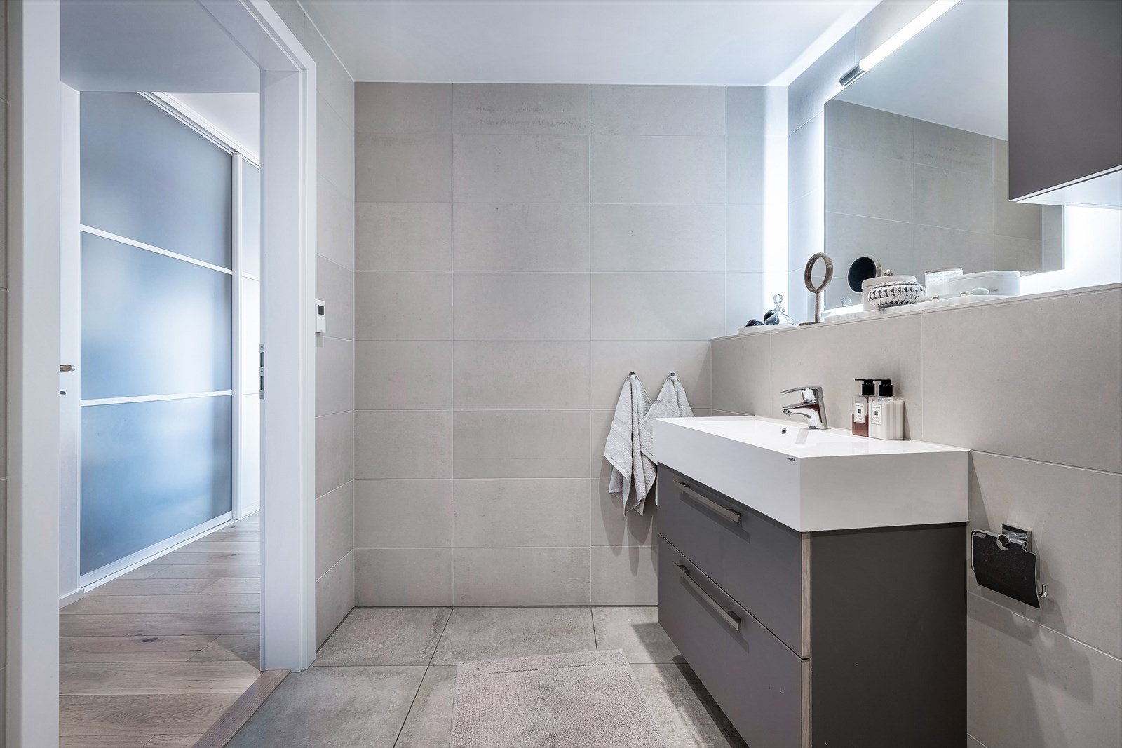 Baderommet har innredning fra HTH og er innredet med servantskap med ett-greps blandebatteri, vegghengt toalett med innebygget sisterne, speil med lys, veggskap, avskjermet dusjhjørne med glass, blandebatteri og dusjgarnityr. Galleribilde