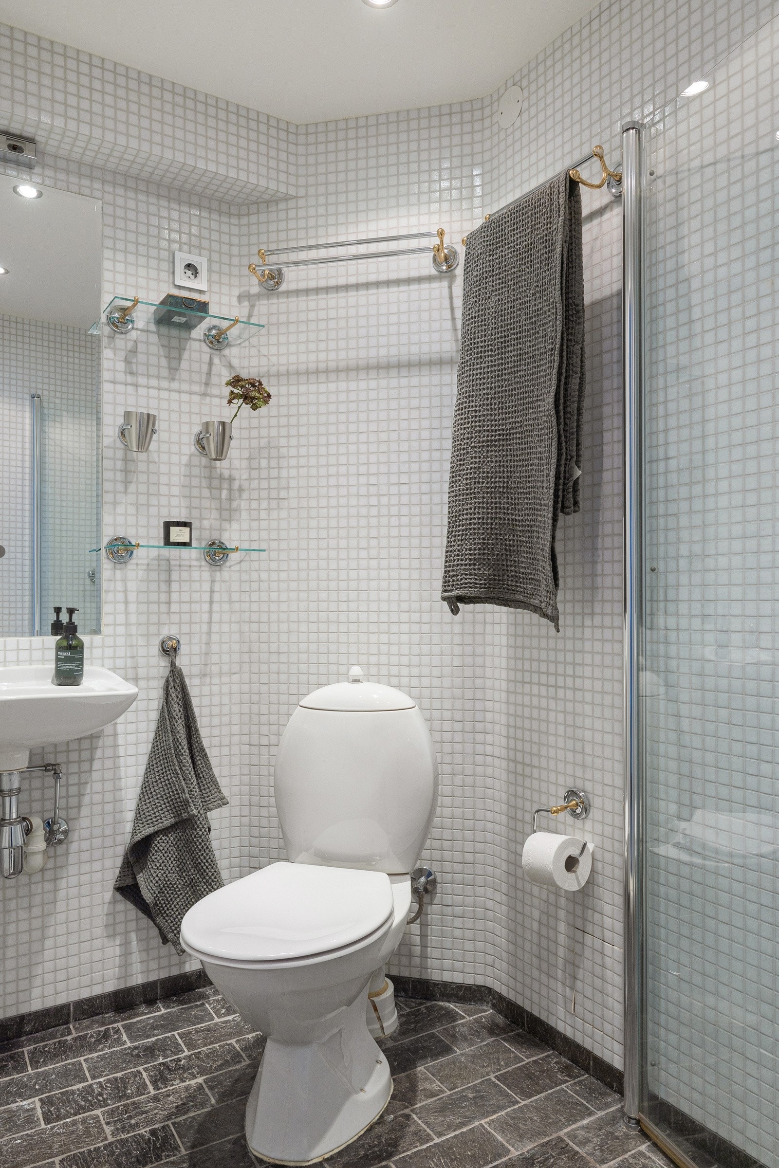 Det minste badet har mørke gulvfliser, hvit mosaikk på veggene, downlights og gulvvarme. Over servanten er det et innmurt speil og ved siden av er det glasshyller. Galleribilde