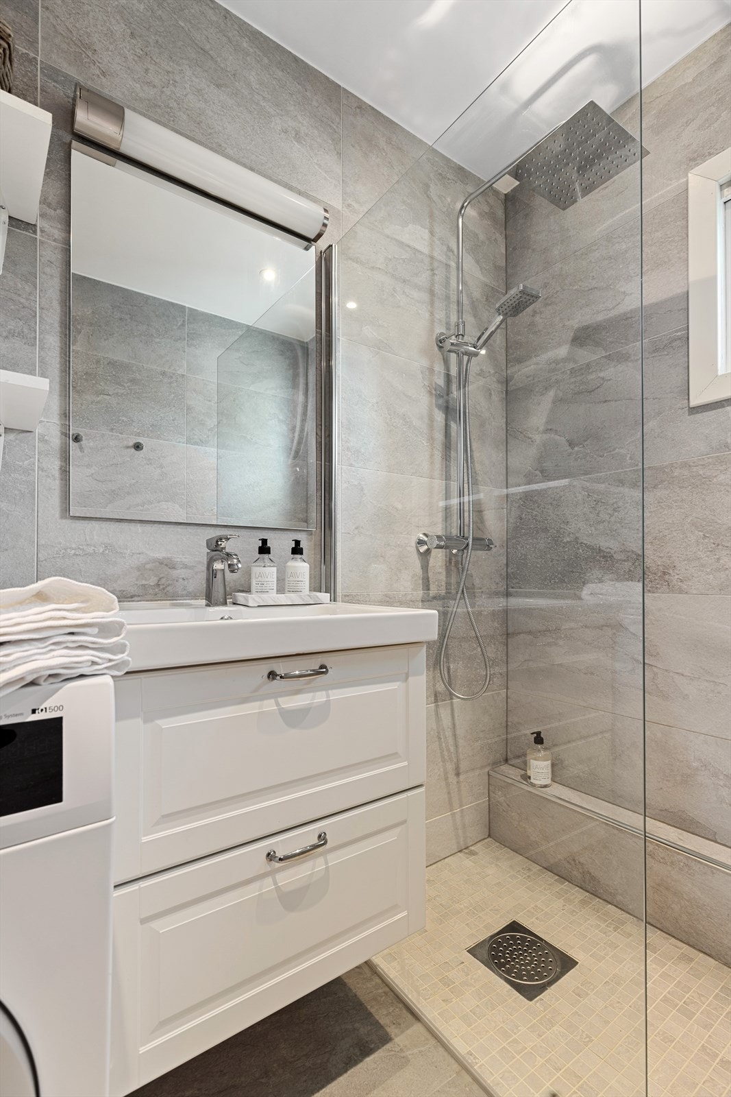 Badet er innredet med veggmontert toalett, servant, dusj og opplegg for vaskemaskin. Galleribilde
