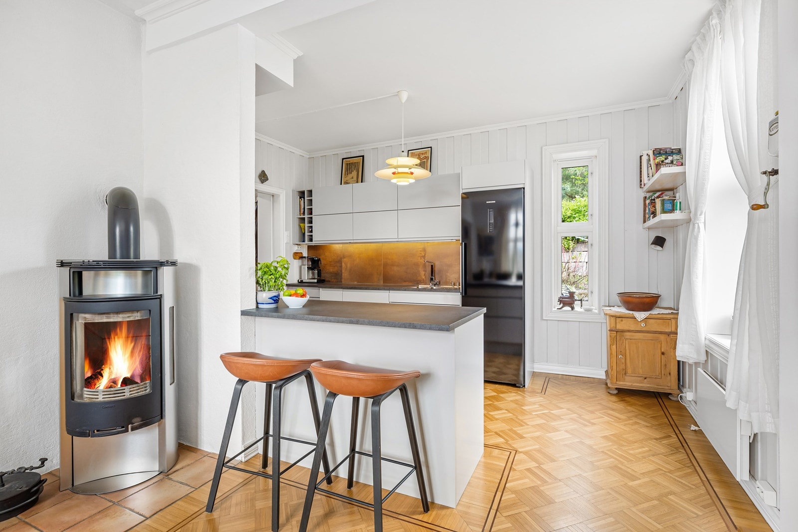 Kjøkkeninnredning med grå glatte fronter og laminert benkeplate. Fliser på vegg mellom kjøkkenbenk og overskap Galleribilde