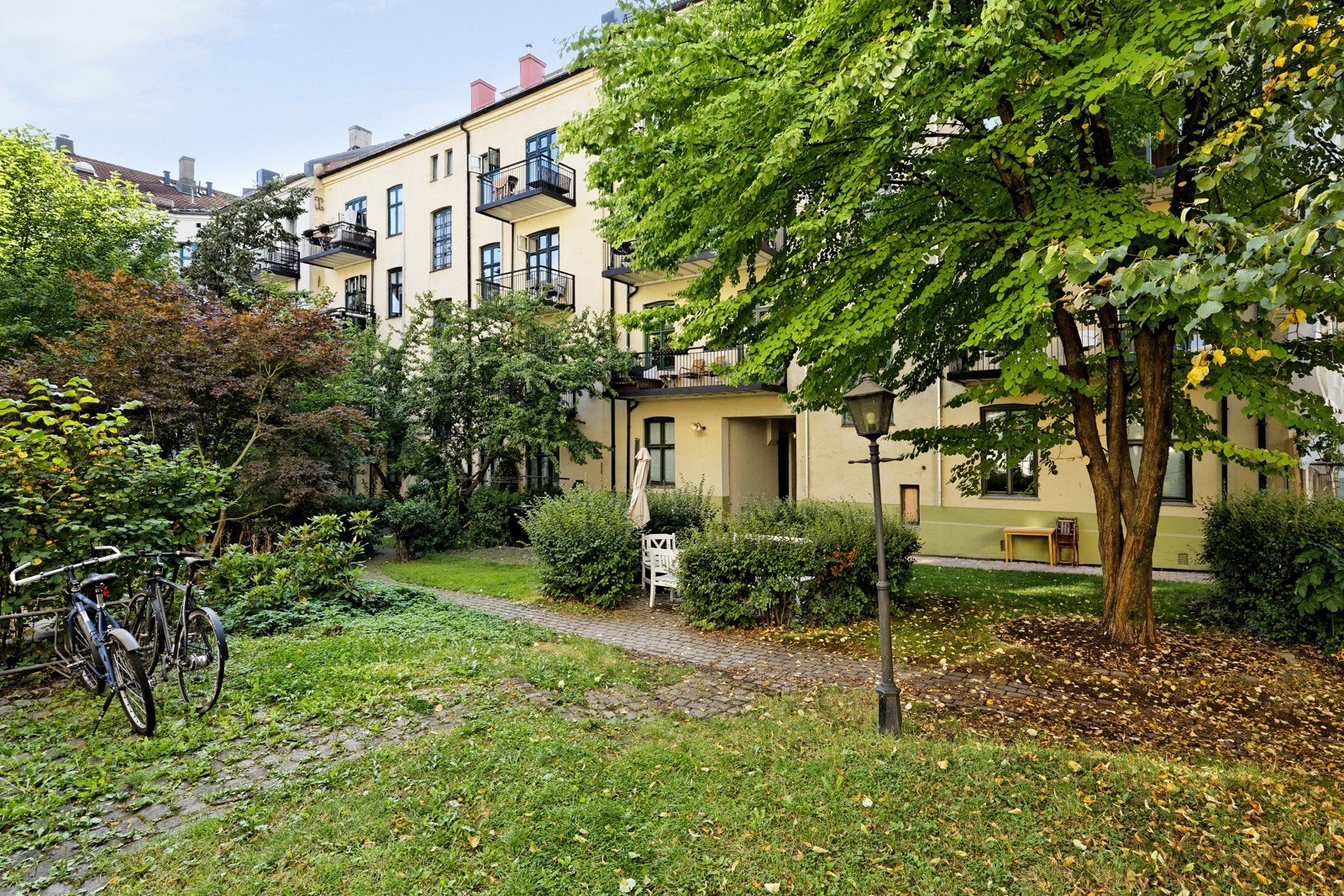 Hyggelig og opparbeidet bakgård med beplantning, trær, gressplen og steinheller Galleribilde