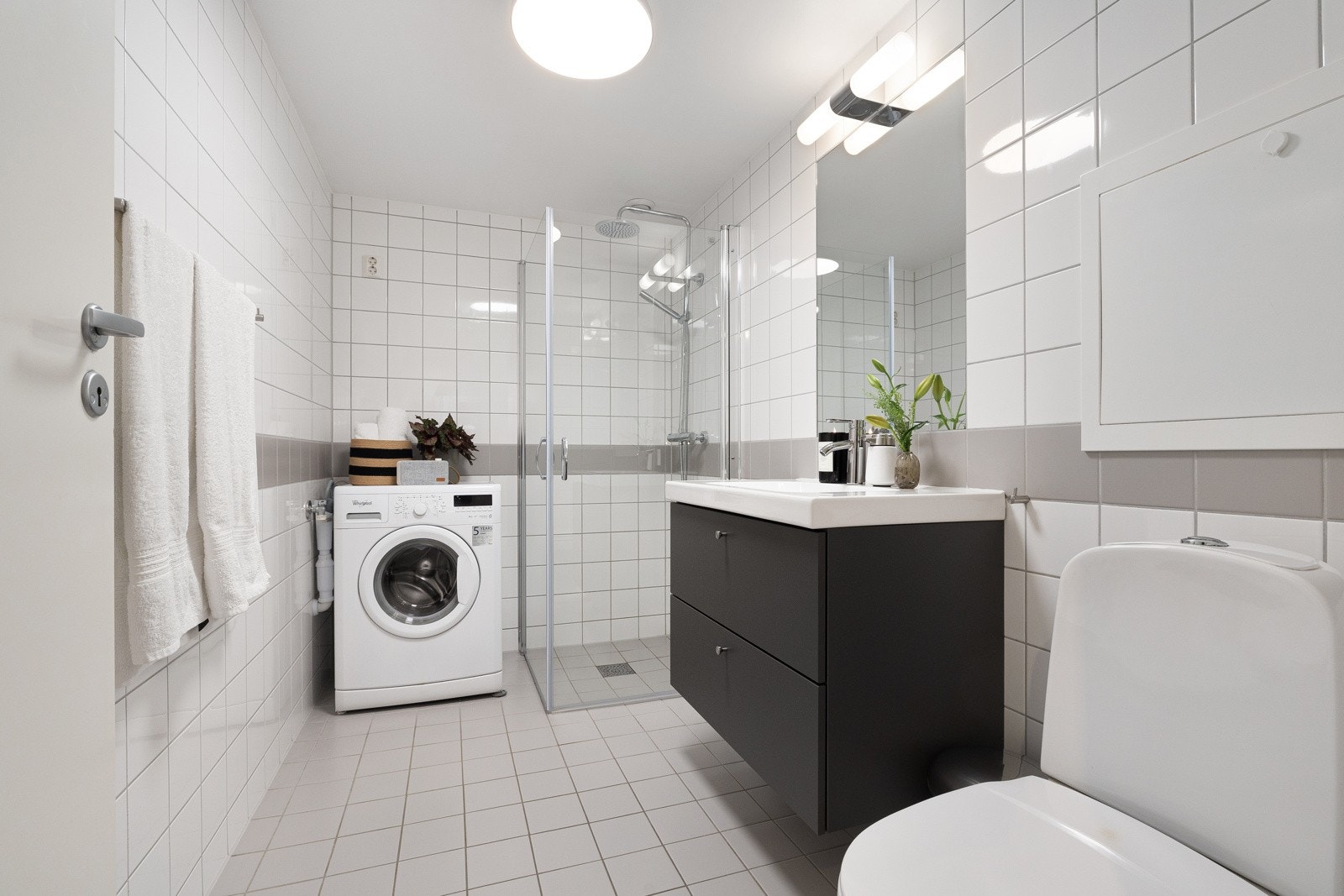 Pent flislagt bad med dusj, toalett, servant med skuffer, innmurt speil, belysning og opplegg for vaskemaskin. Galleribilde