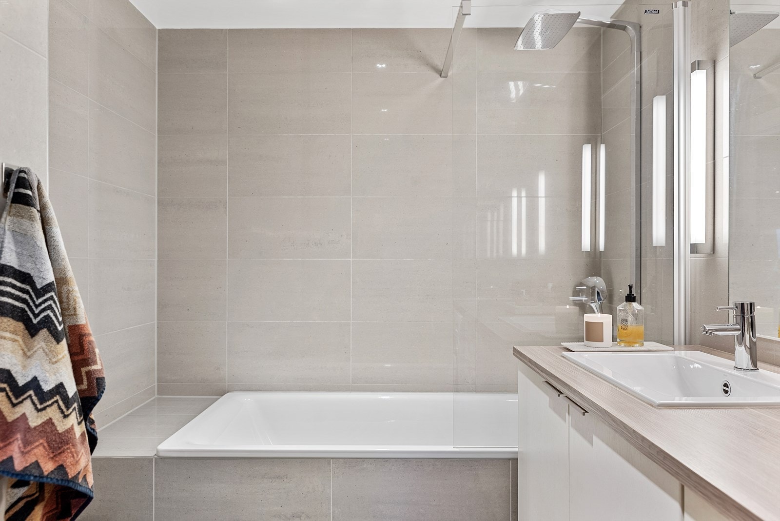 Moderne flislagt bad innebygget badekar med dusjvegg i glass og dusjarmatur (håndholdt og regnfall). Galleribilde