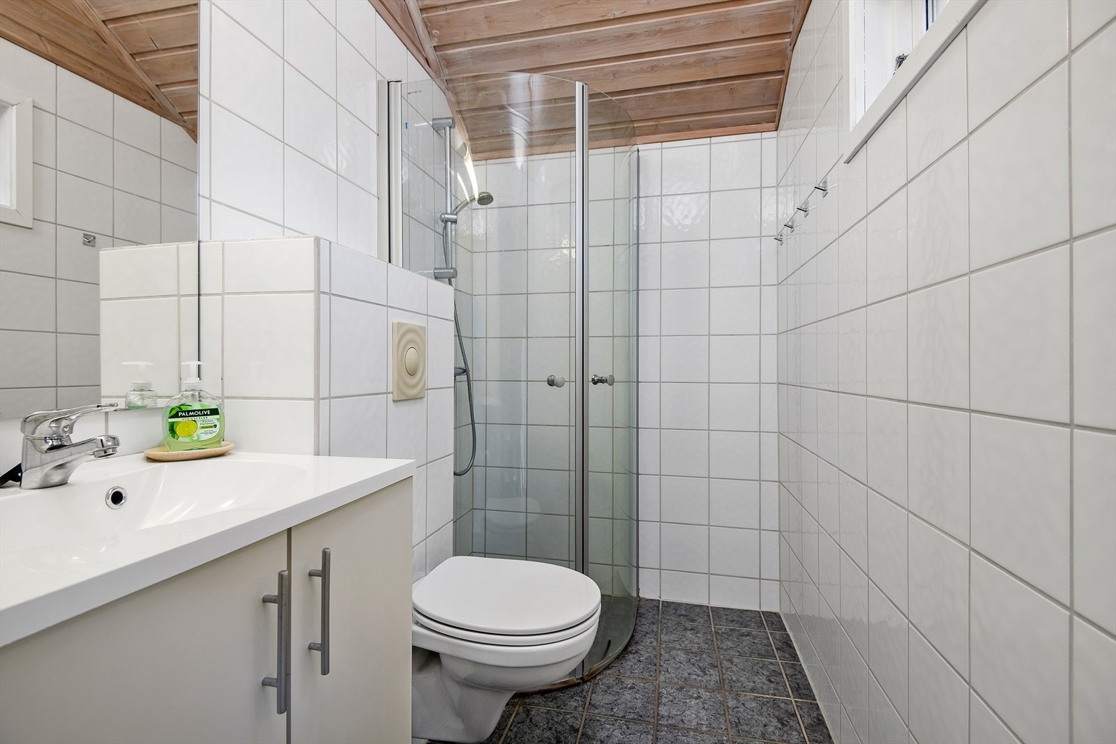 Vegghengt WC. Dusjen har innfellbare glassdører. Innredningen har skap for oppbevaring under servant. Galleribilde